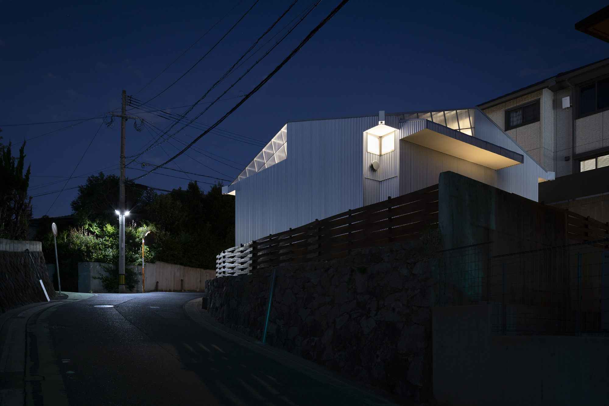 Uphill street approach with timber retaining wall and overhead power lines at night