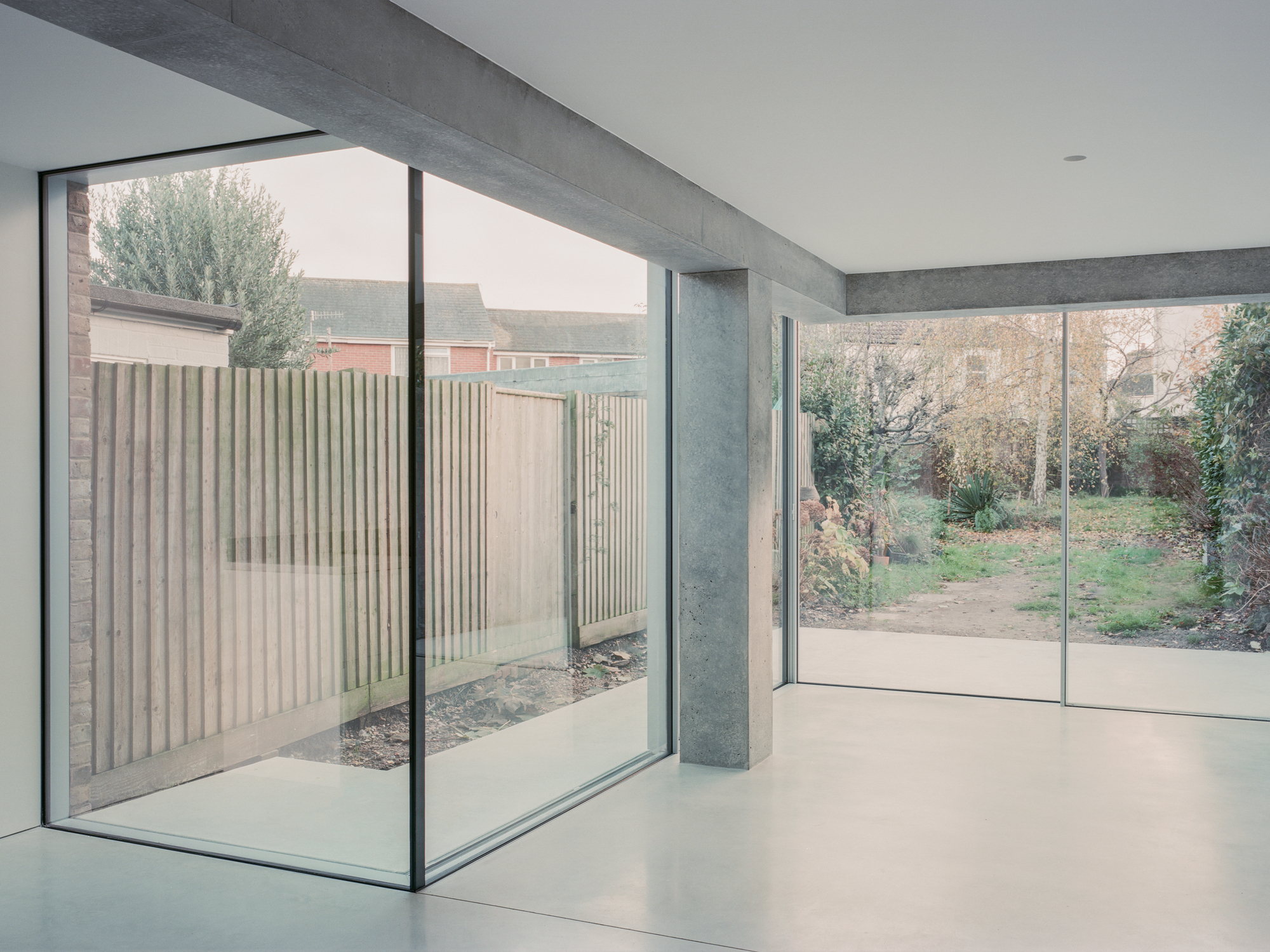 Interior corner with full-height glazing framing a timber-slatted fence and bare winter garden