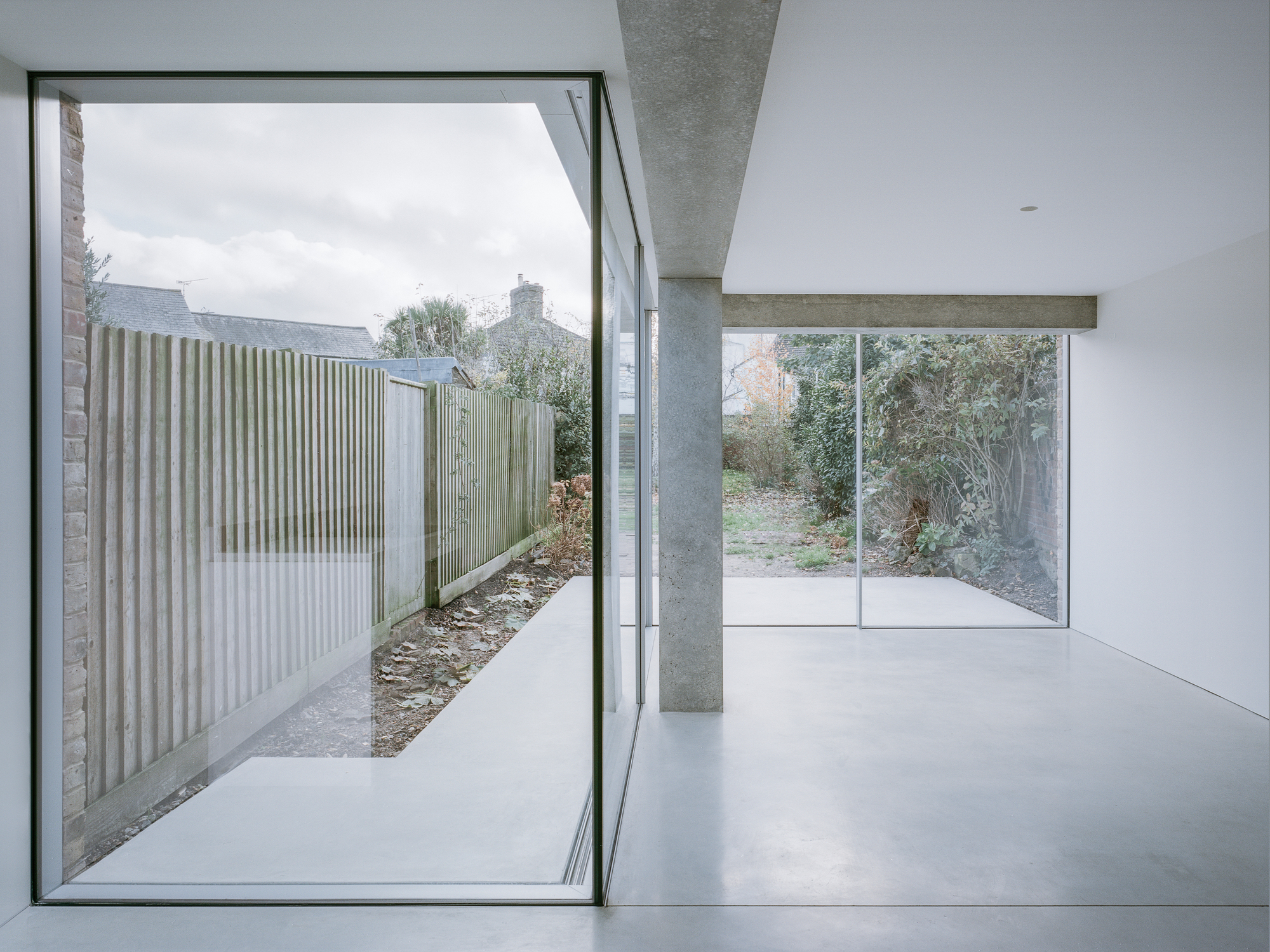 White interior room with exposed concrete beam, cruciform column and sliding glass doors to garden courtyard