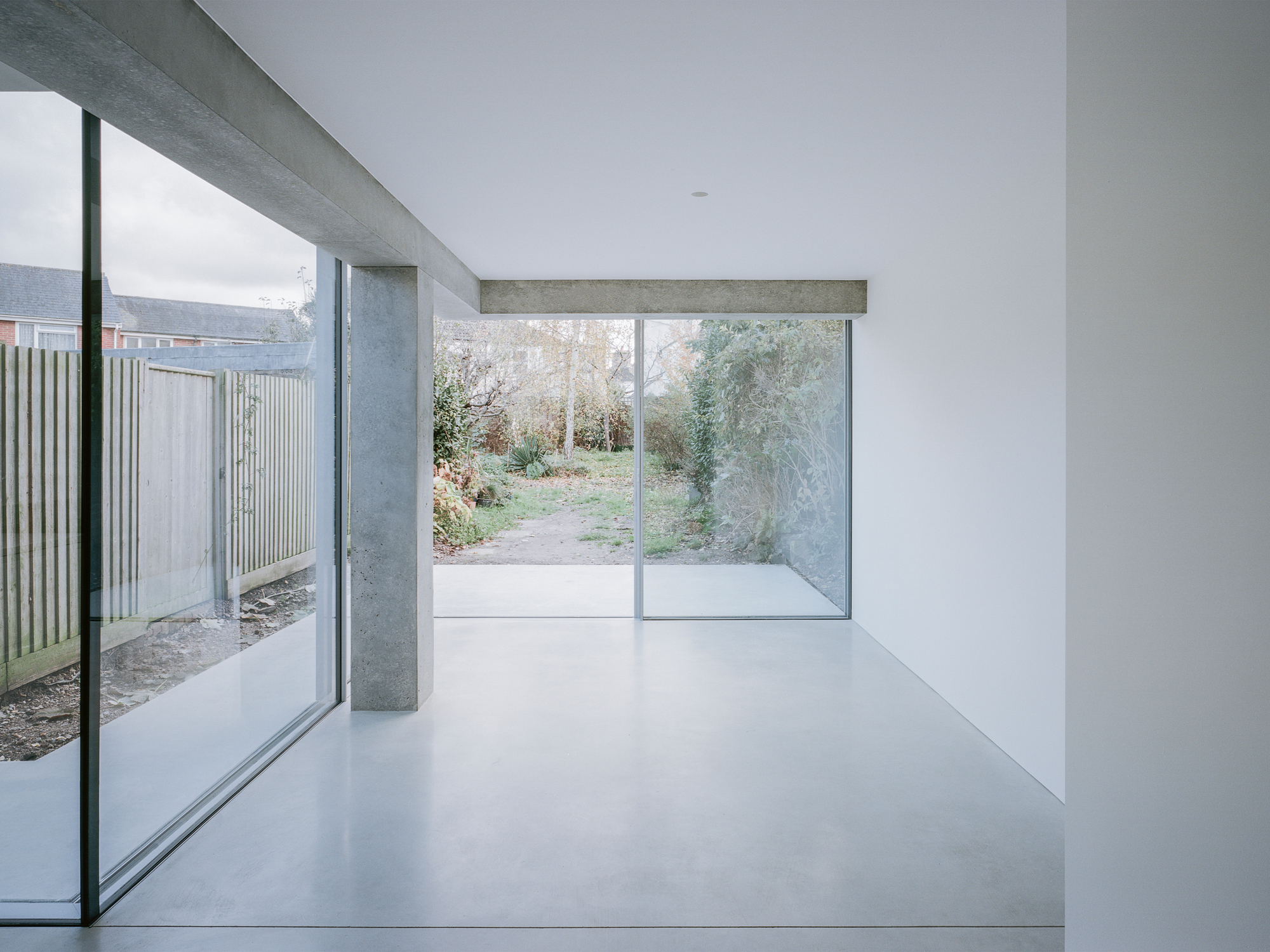 Polished concrete floor meeting perpendicular glazed walls that open onto planted garden pathways