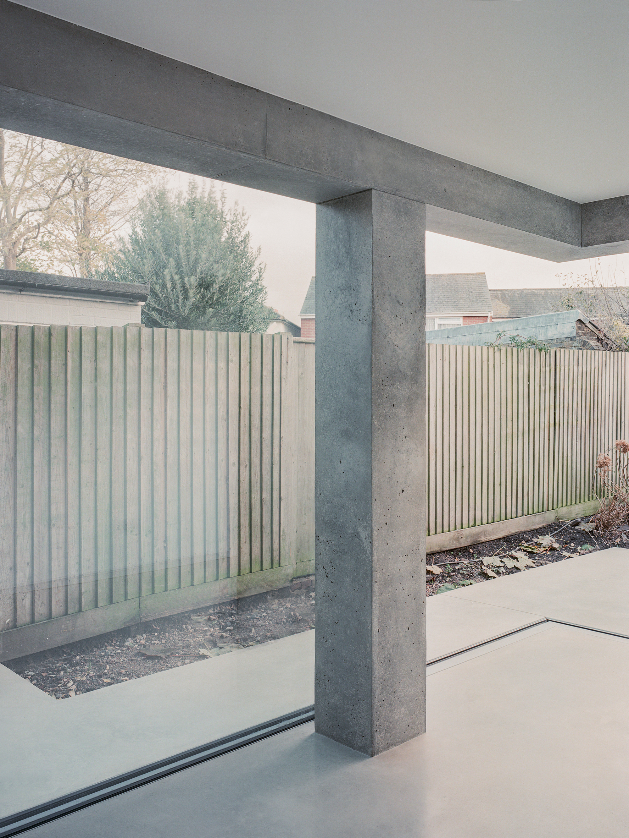 Concrete column and beam frame in courtyard with vertical timber fence panels and gravel planting beds