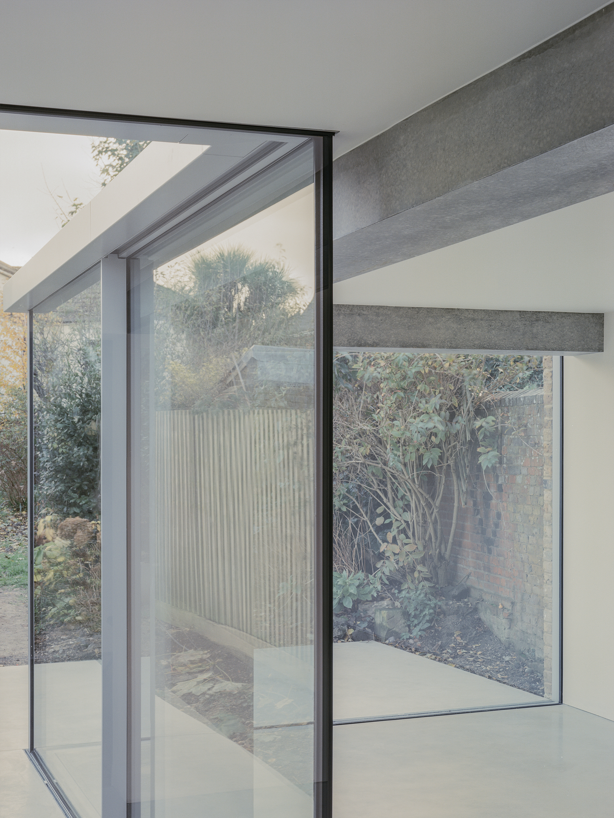 Floor-to-ceiling glazing framing the courtyard with exposed concrete beams and planted garden beyond