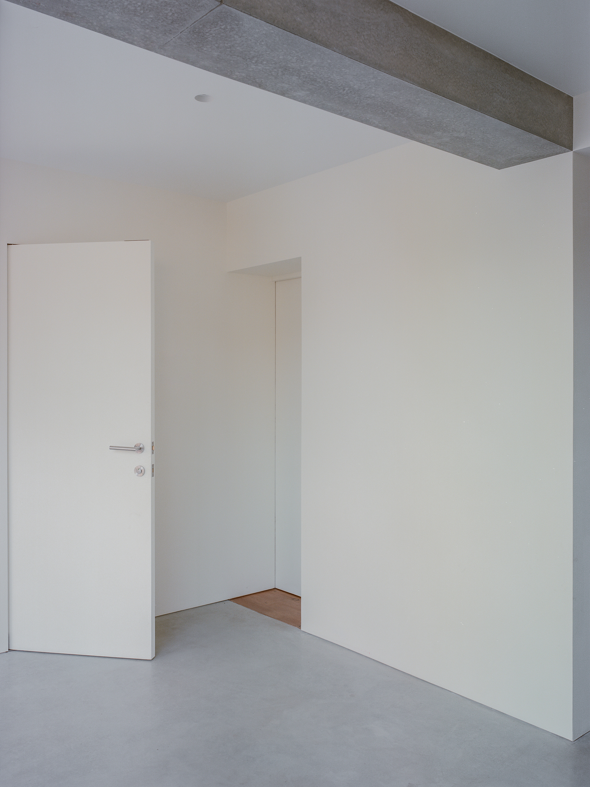 White plastered interior walls with flush doors and exposed concrete ceiling beam