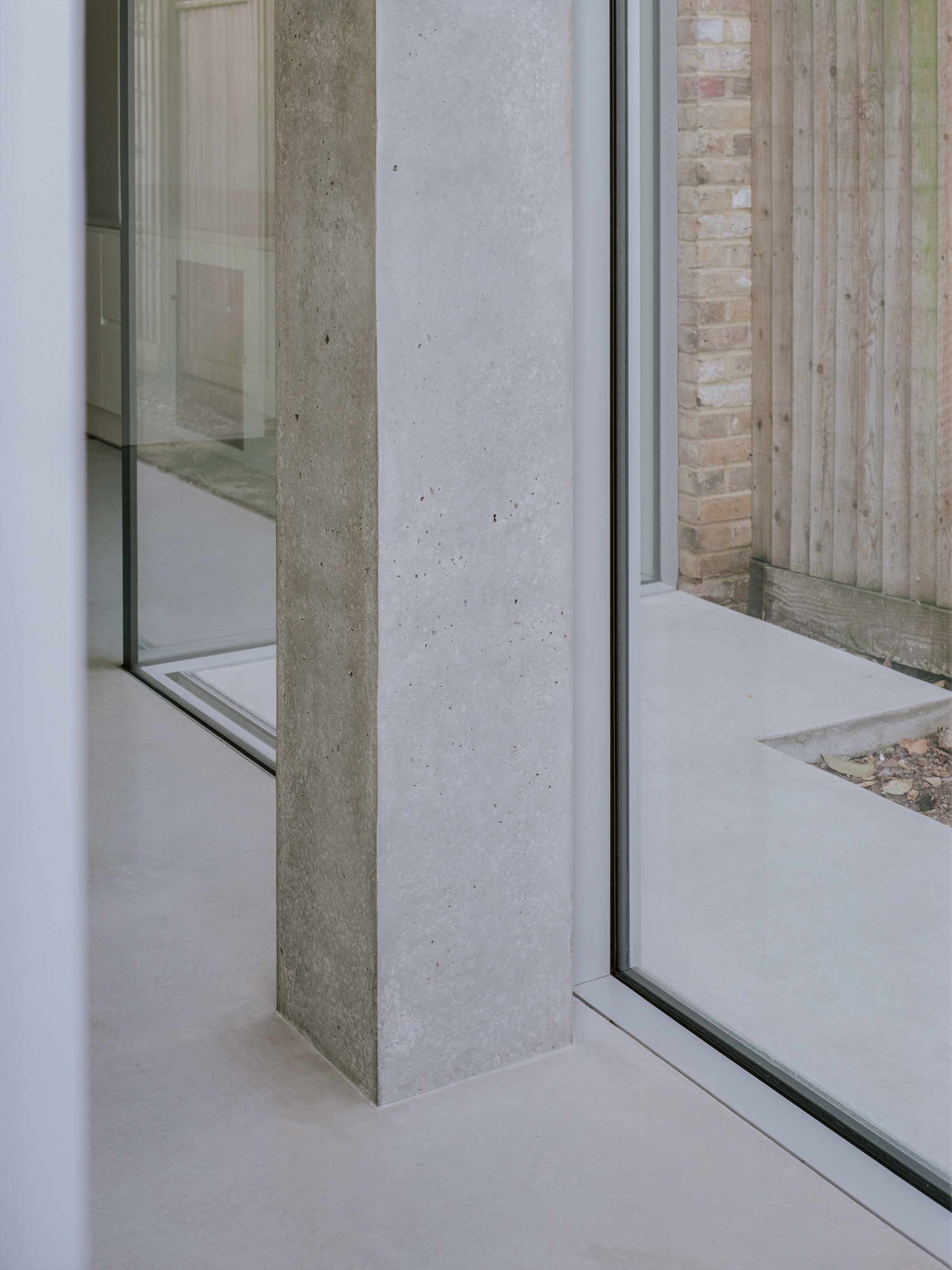 Detail of concrete column meeting glass corner with timber fence and courtyard visible outside