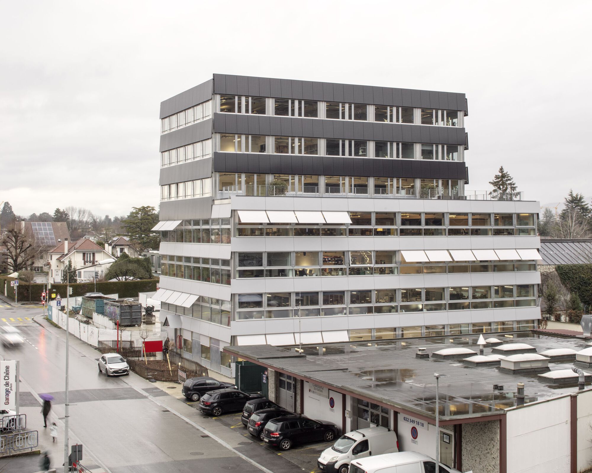 Stacked office volumes with horizontal bands of windows and projecting awnings on an overcast day