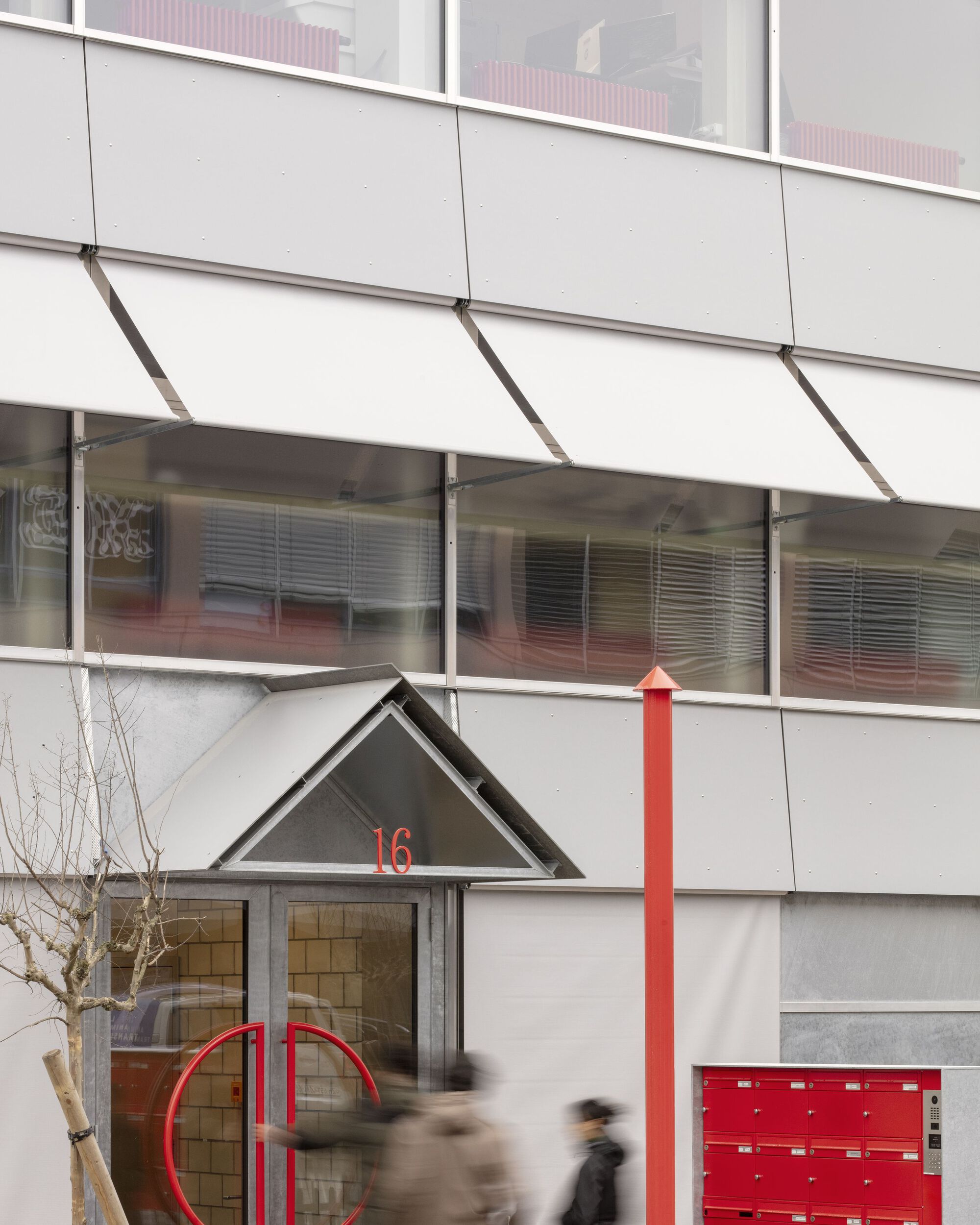 Ground floor entry with triangular canopy, red mailboxes, and blurred pedestrians passing by