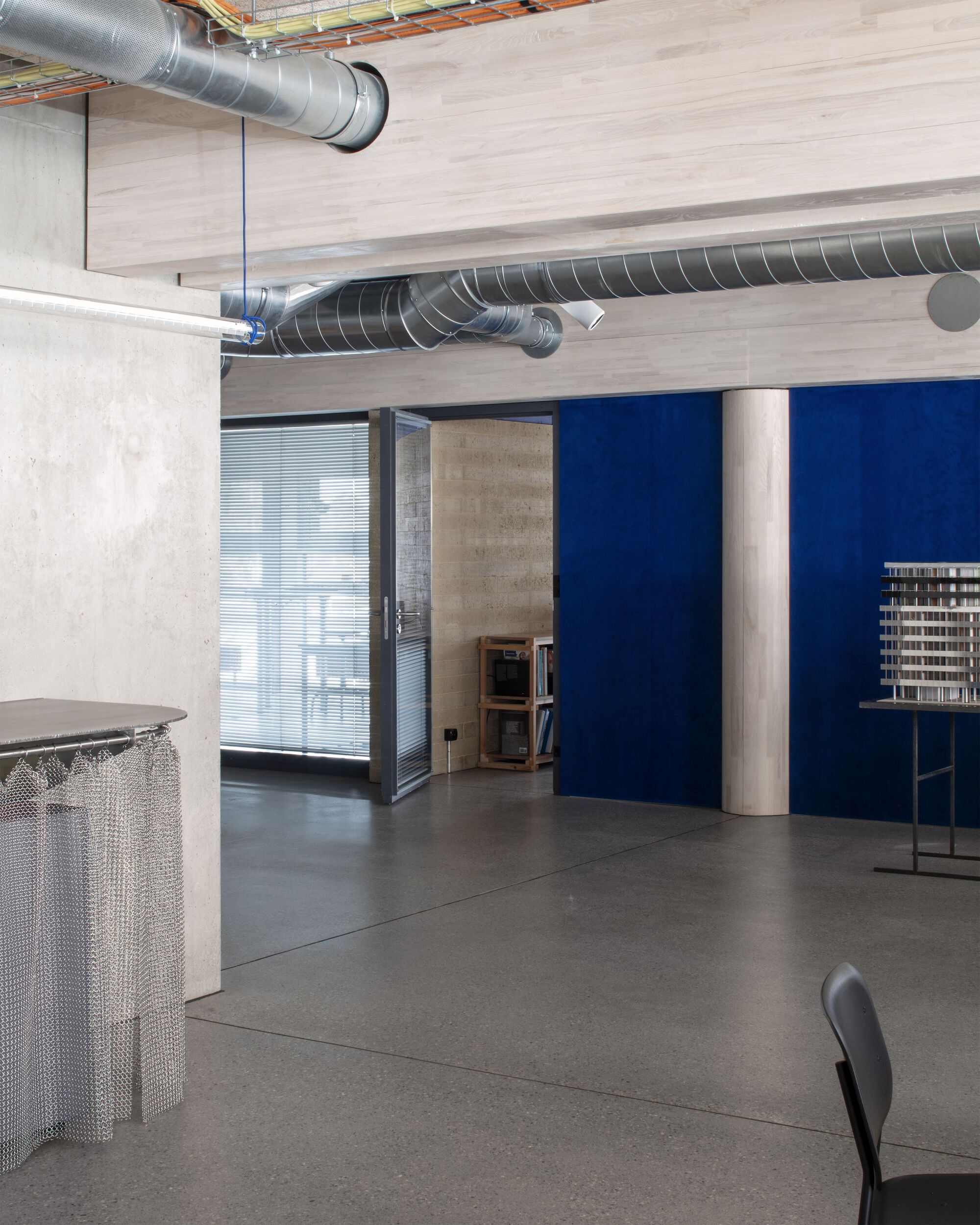 Office interior with exposed spiral ductwork, concrete walls, and blue partition separating work areas