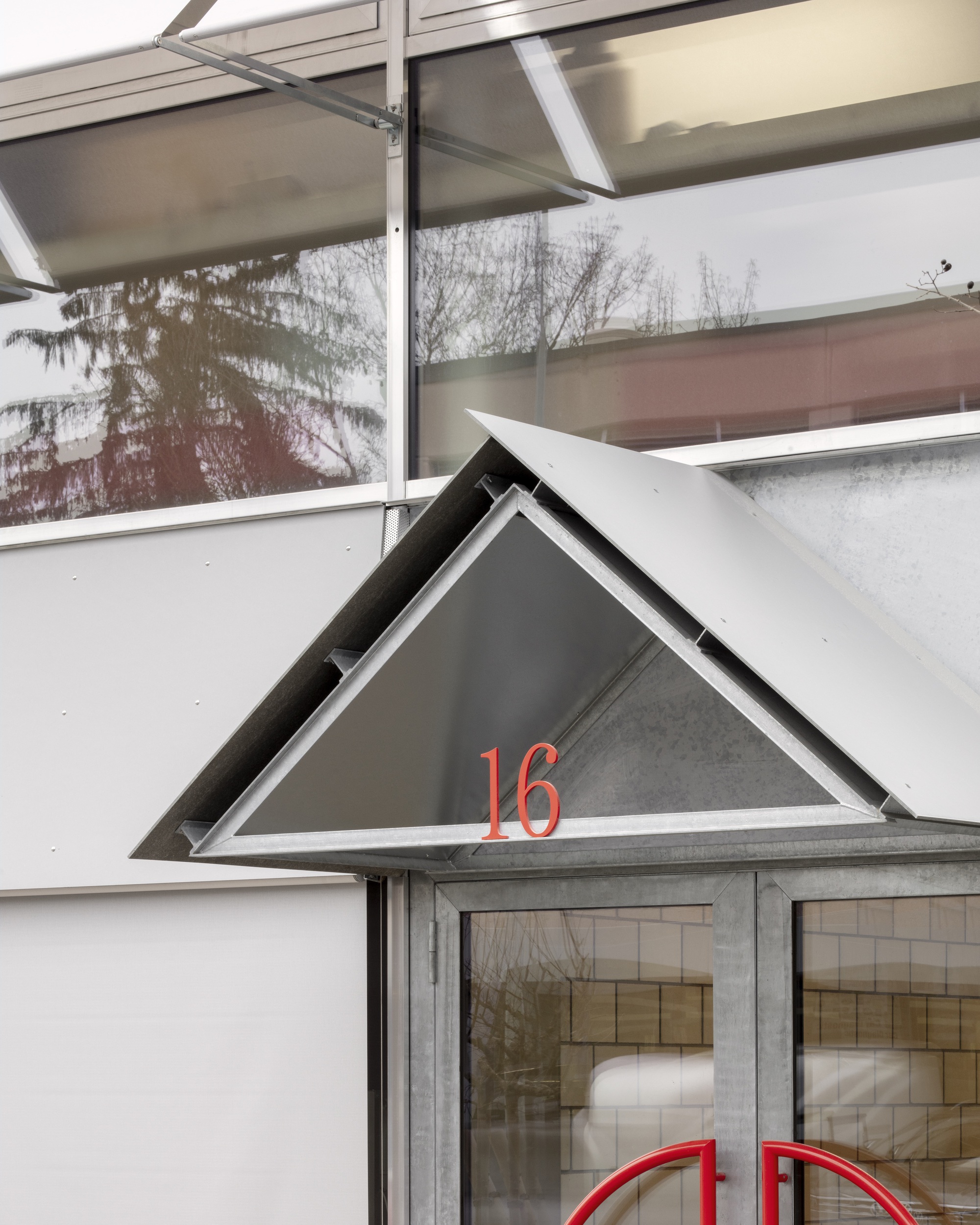 Triangular entry canopy with red numbering above glazed doors and recessed signage