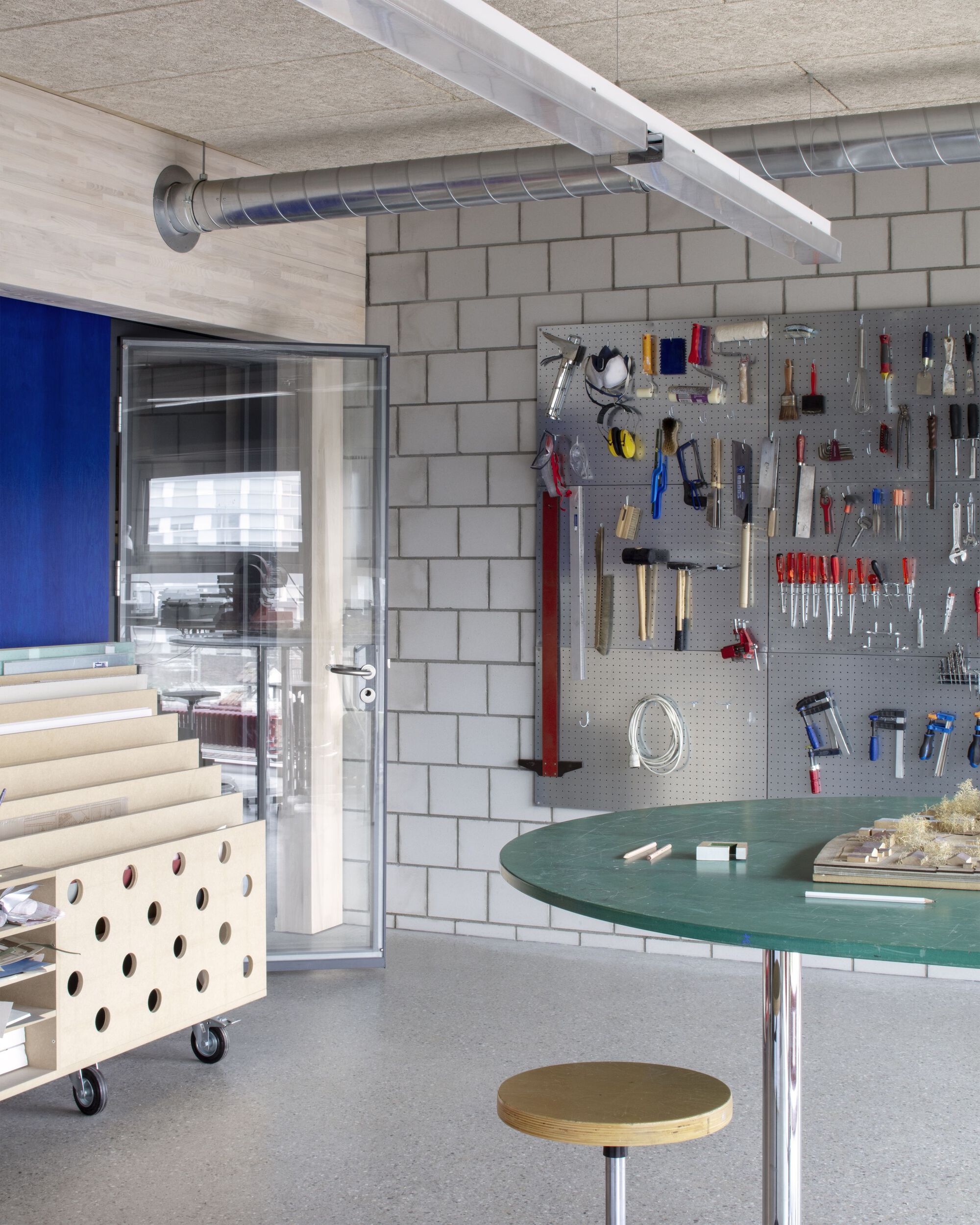 Workshop area with pegboard tool wall, round green work surface and concrete block partition