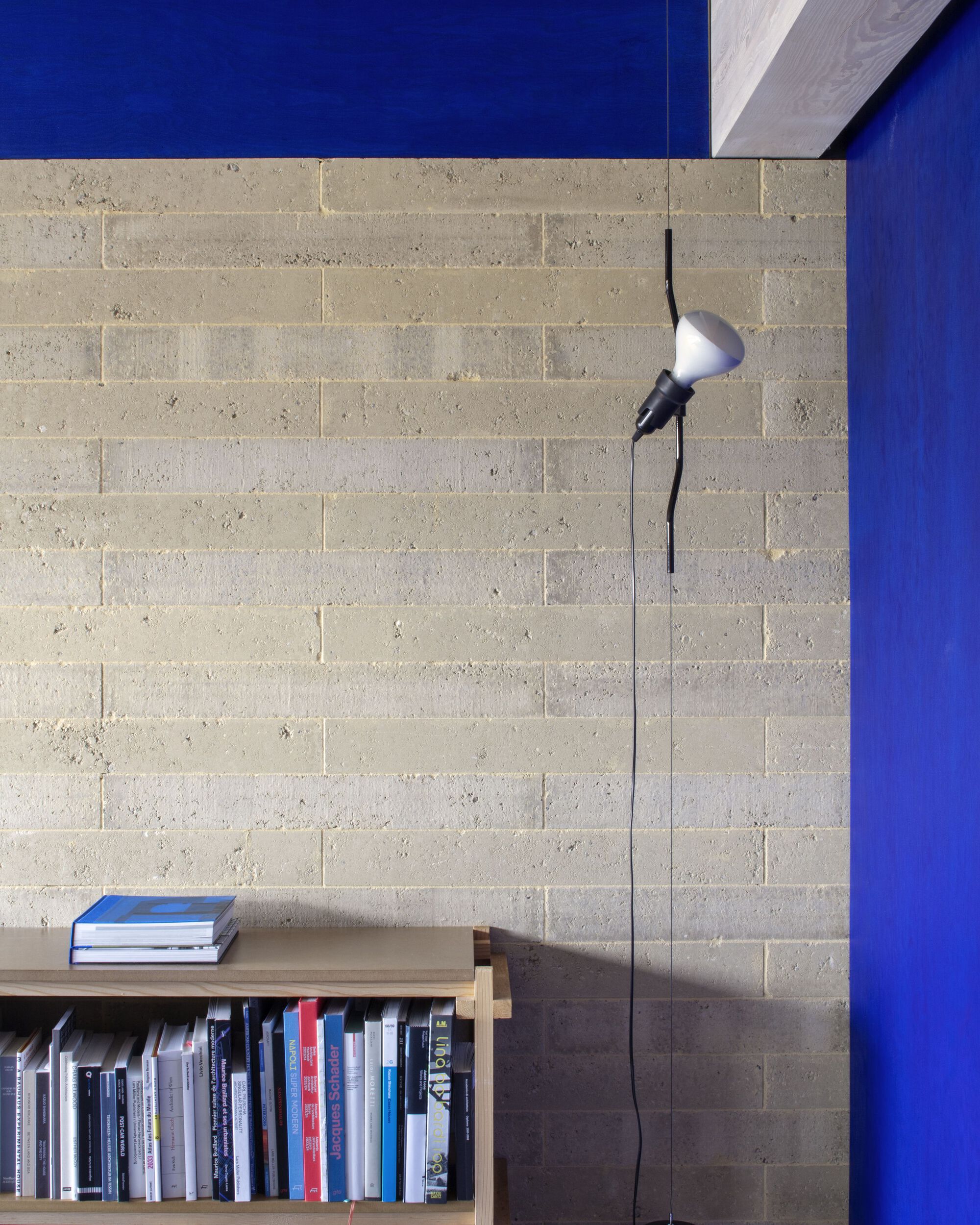 Concrete block wall with low bookshelf and articulated wall lamp against a blue painted surface
