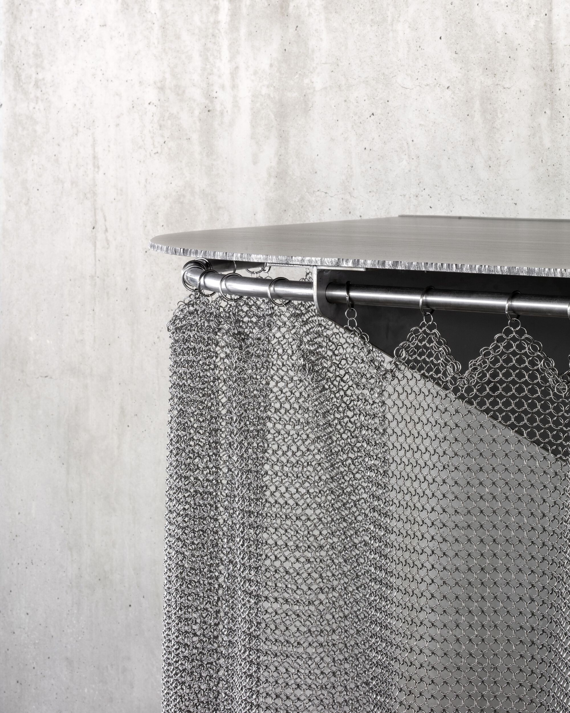 Close-up of chainmail curtain hanging from steel rod beneath a timber shelf edge