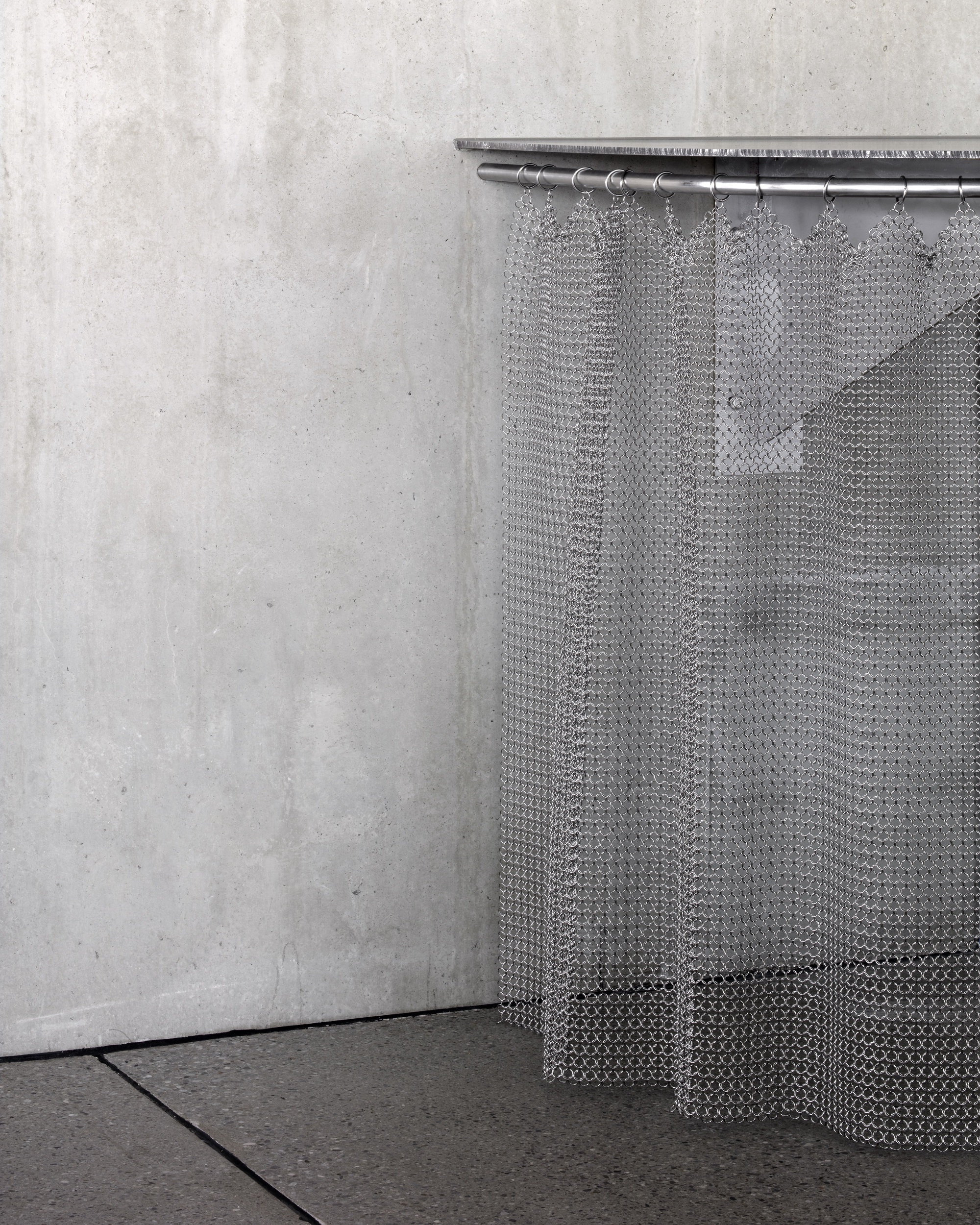 Metal mesh curtain suspended from rod in corner against poured concrete wall