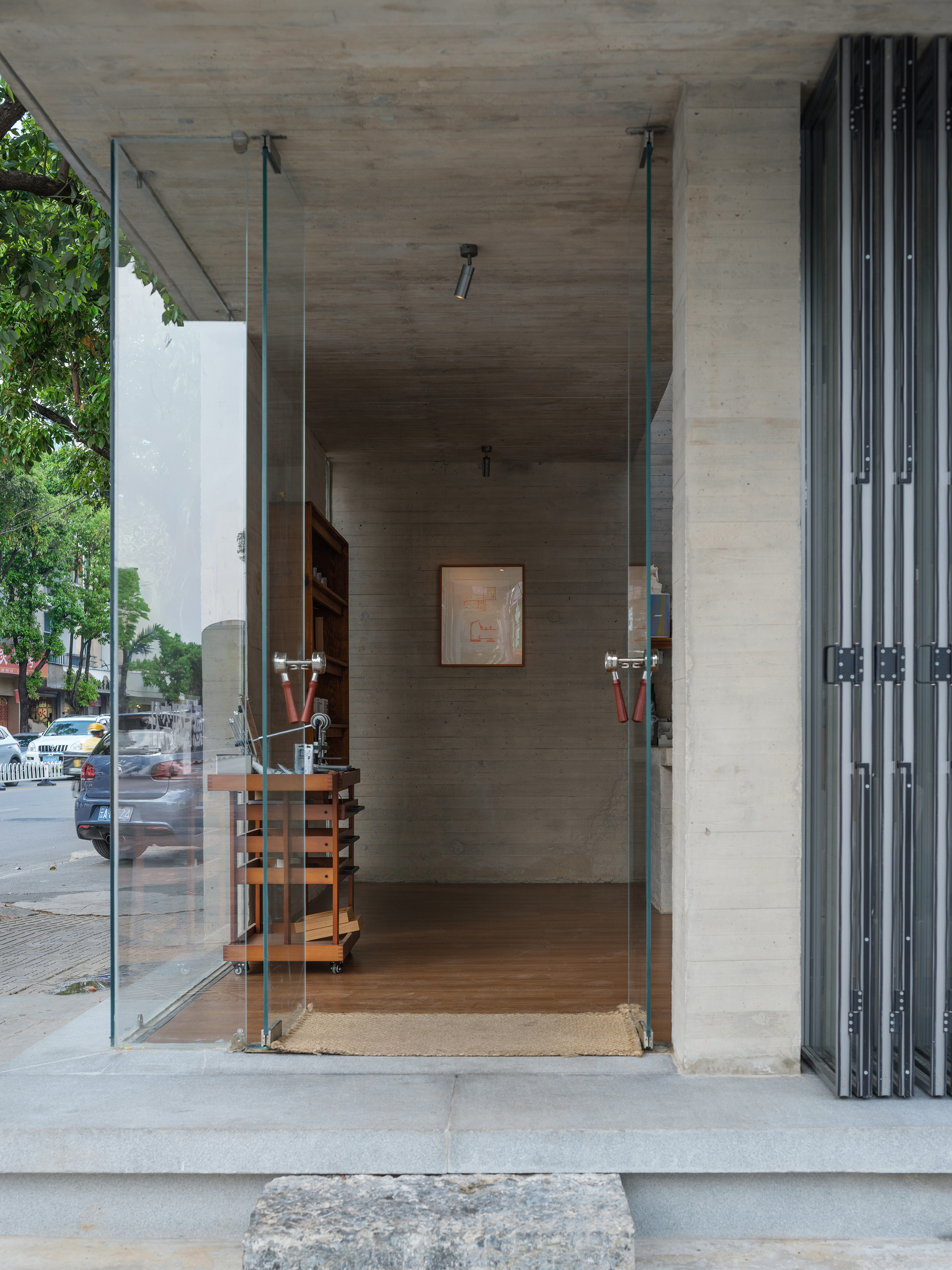 Glass pivot door entrance with timber furniture visible through board-formed concrete threshold