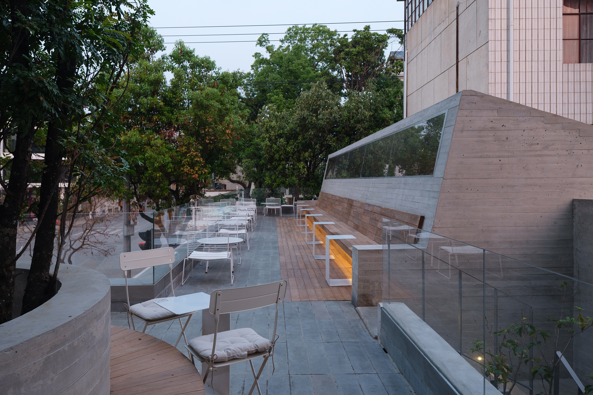 Rooftop terrace with timber decking and glass balustrade overlooking trees at dusk