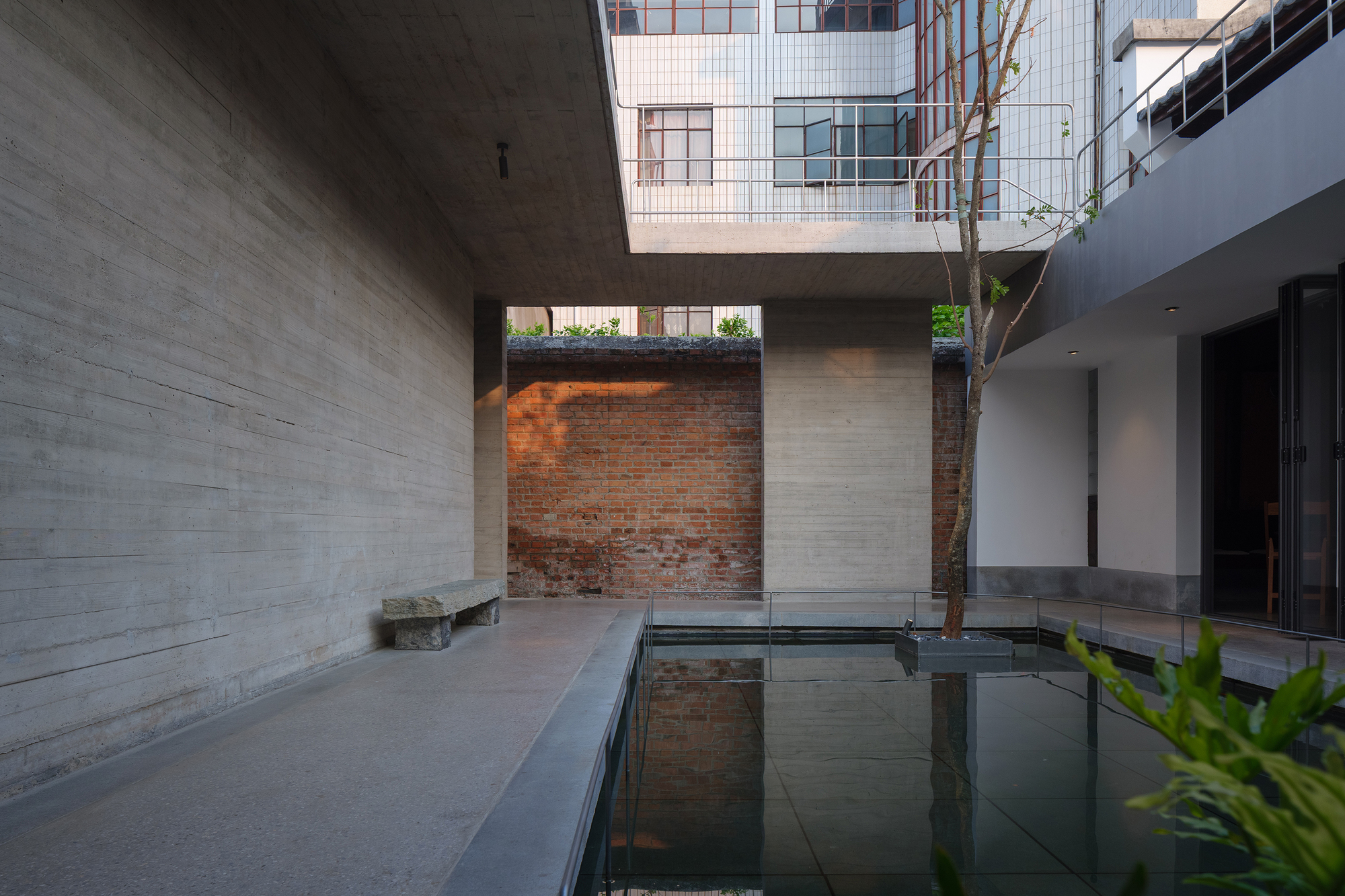 Courtyard water feature with exposed brick wall and tree trunk framed by concrete volumes