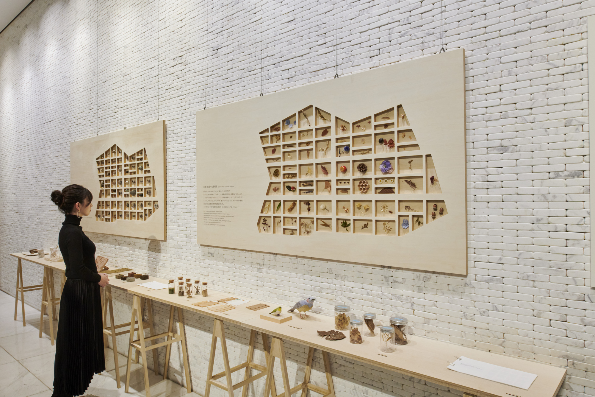 Interior gallery wall with two house-shaped display cases holding samples above a timber trestle table