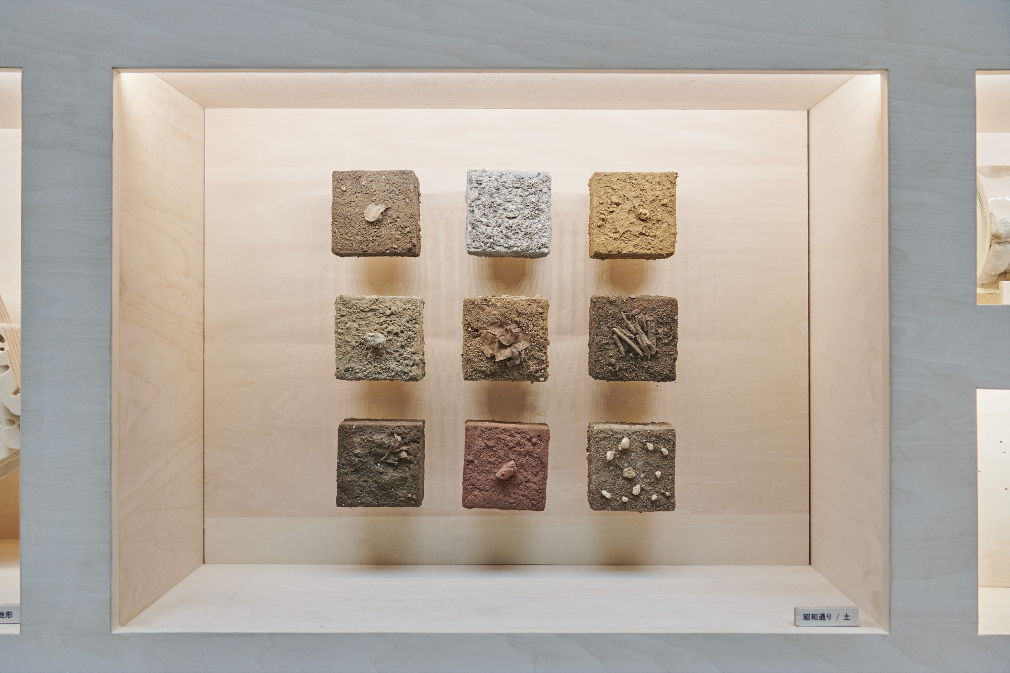 Nine textured earth and stone sample cubes arranged in a grid within a pale timber display box