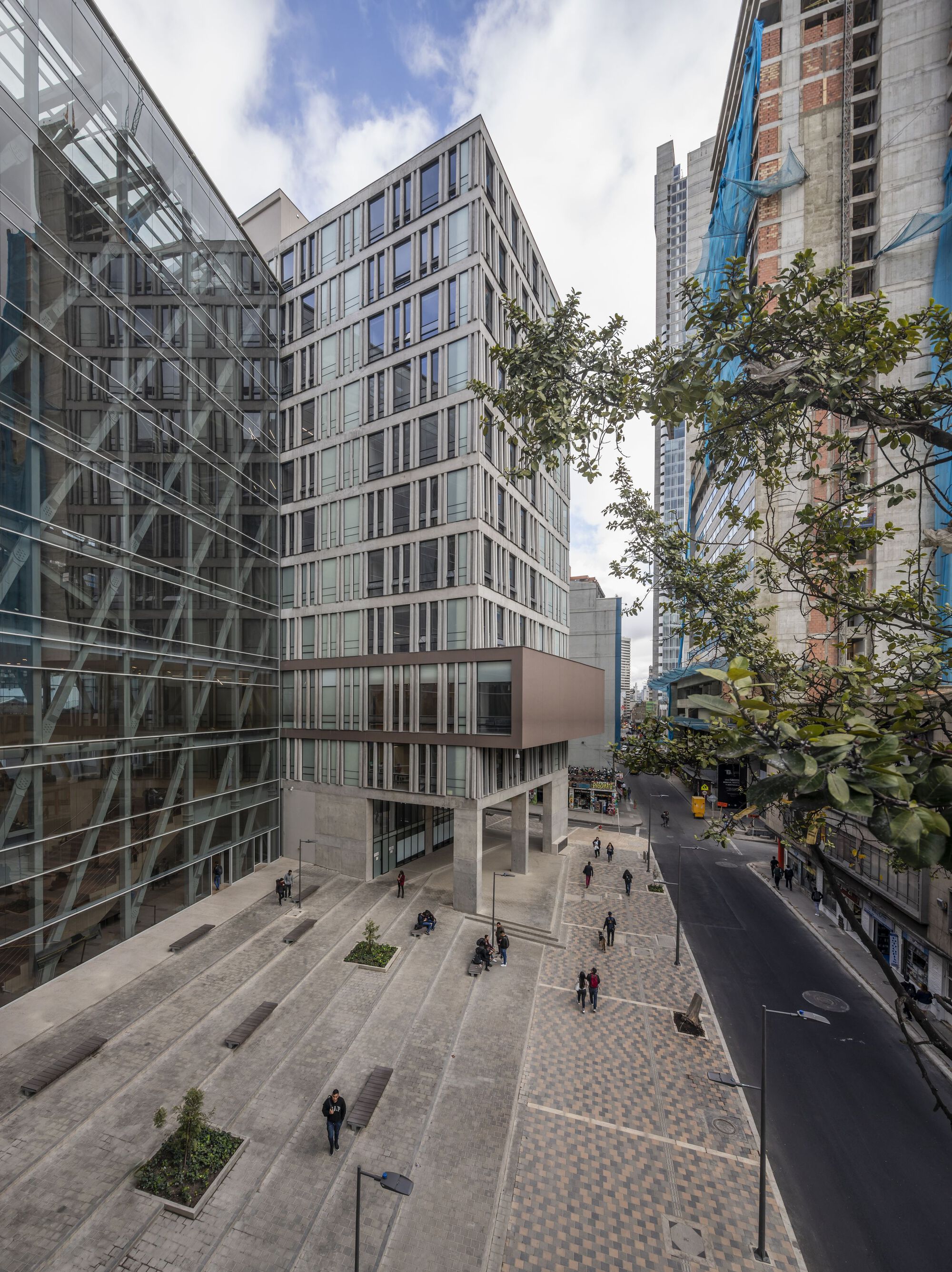 Public plaza with patterned paving and planted beds beneath the paired office blocks and courtyard tree