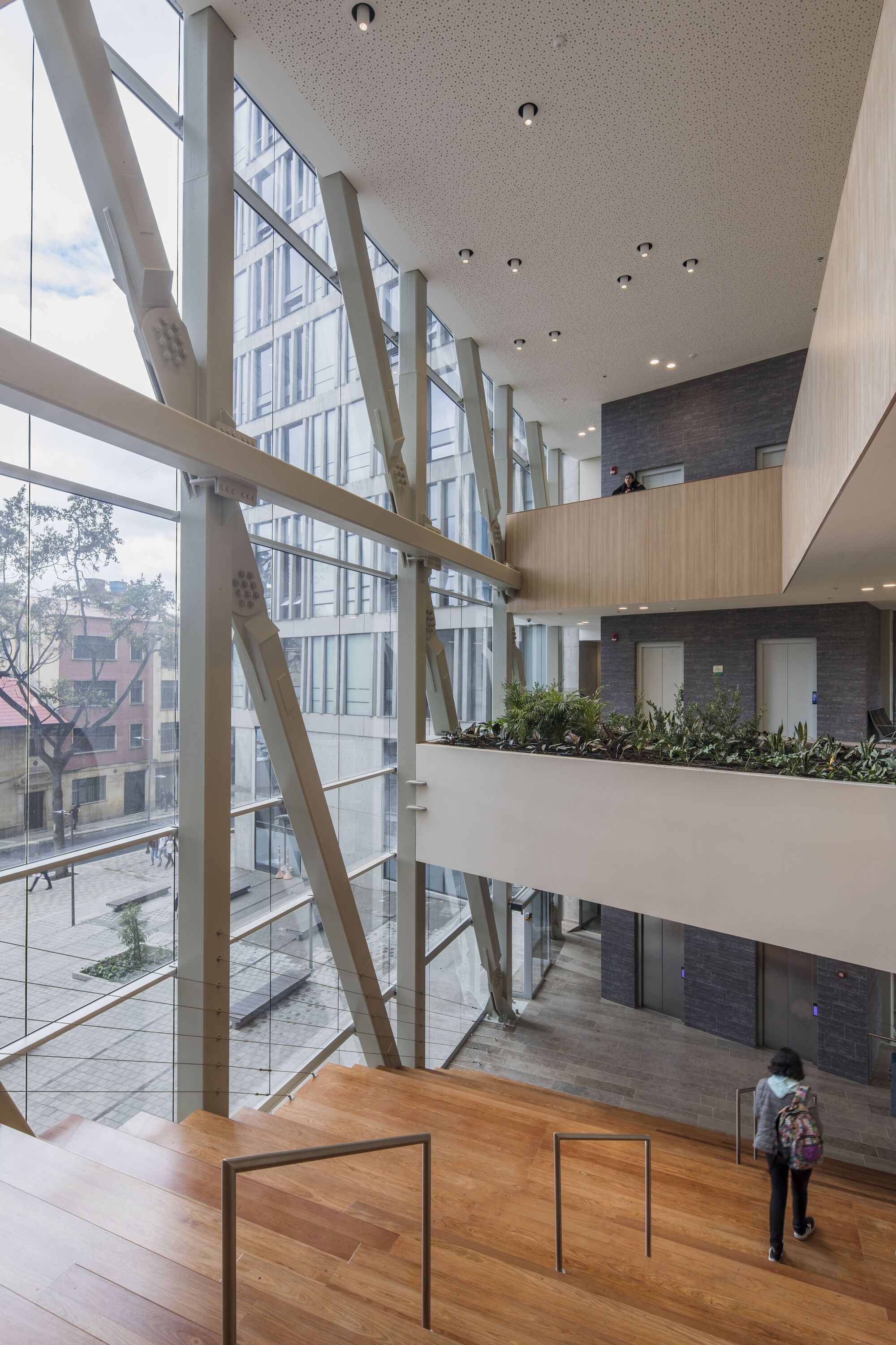 Interior atrium with diagonal white bracing members along the glazed curtain wall and planted upper balcony