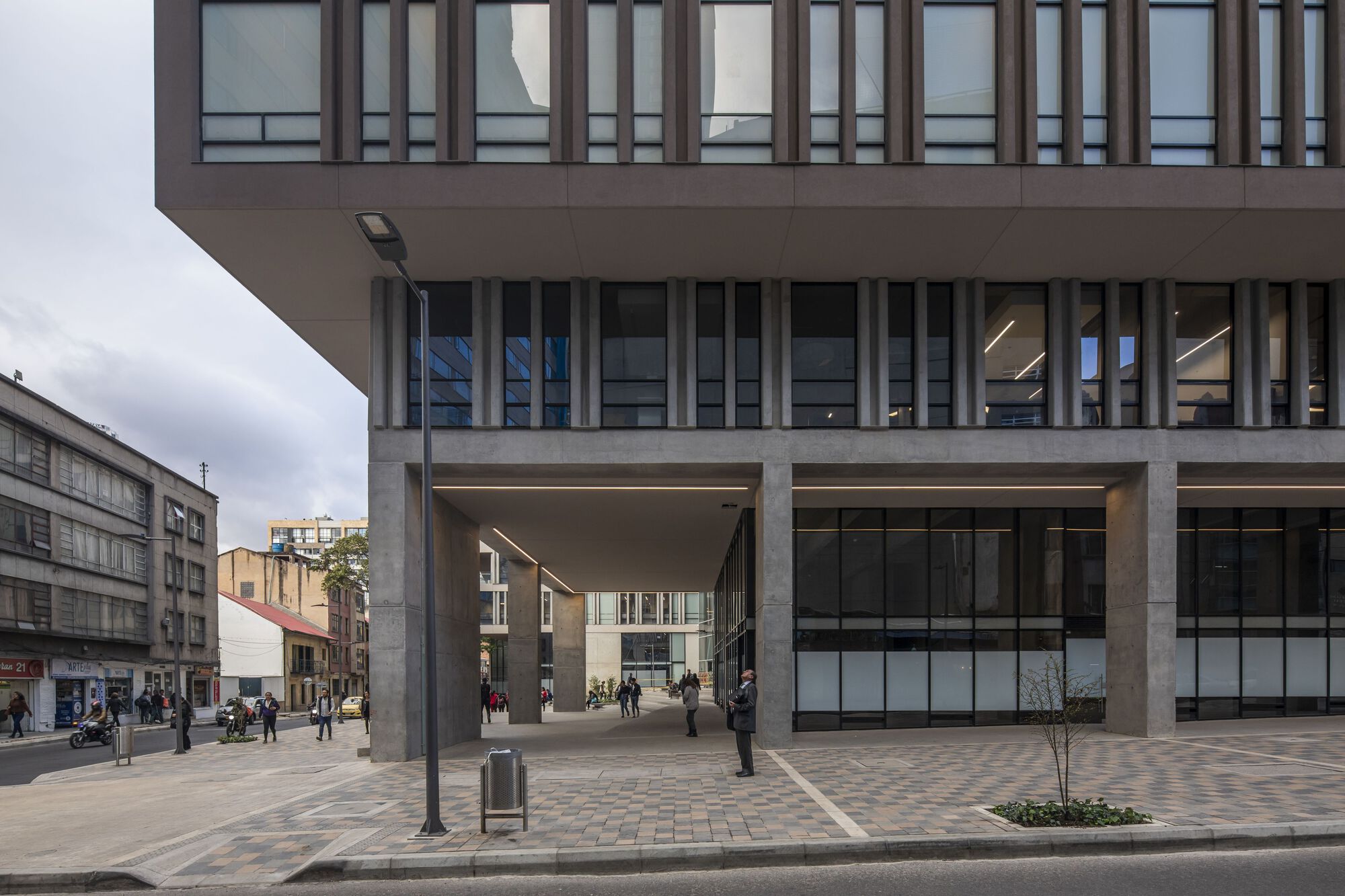 Street view of the raised concrete structure with a large passthrough opening to the plaza beyond