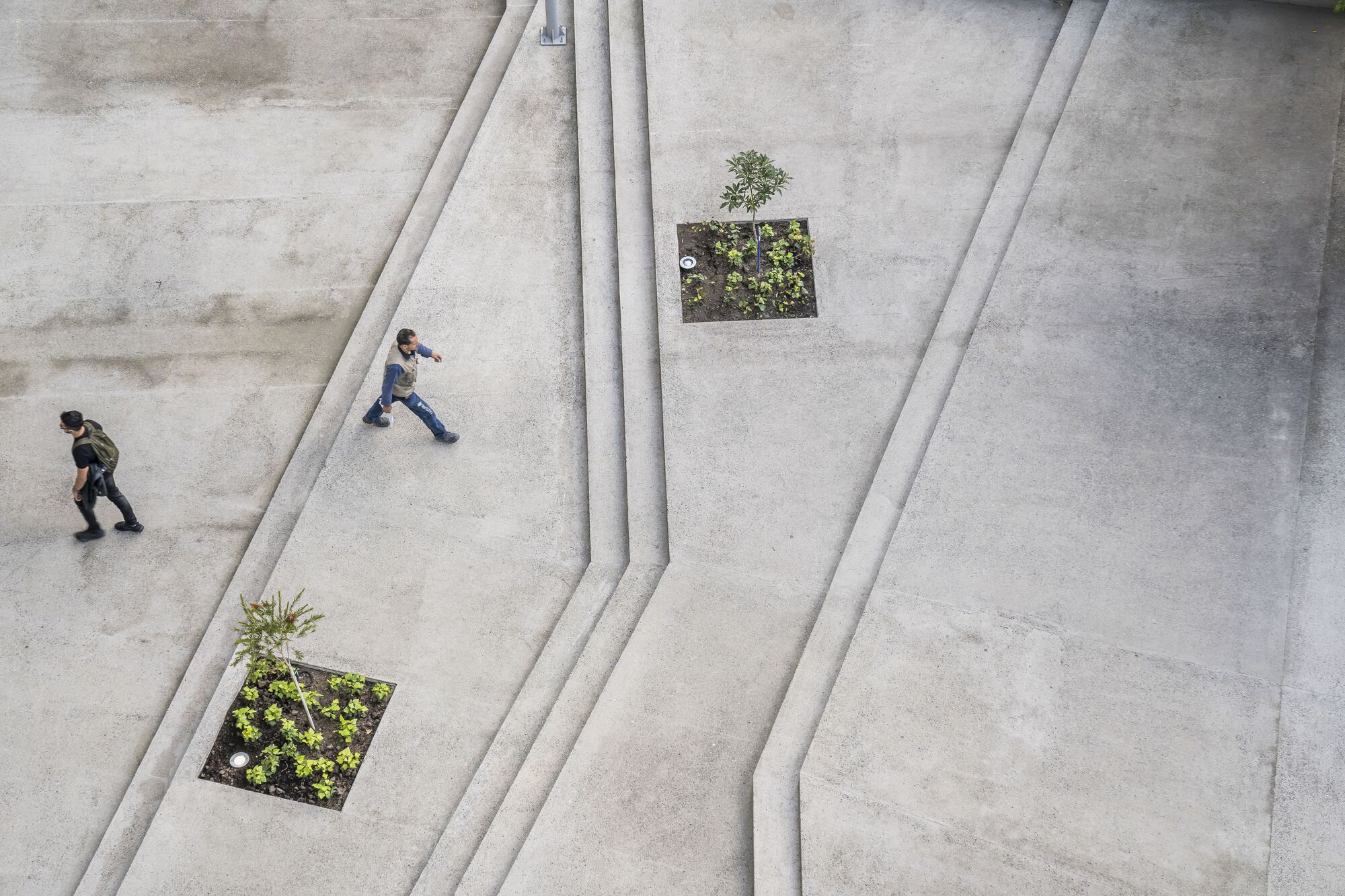 Overhead view of the concrete plaza with angled relief channels and planted beds with two people walking