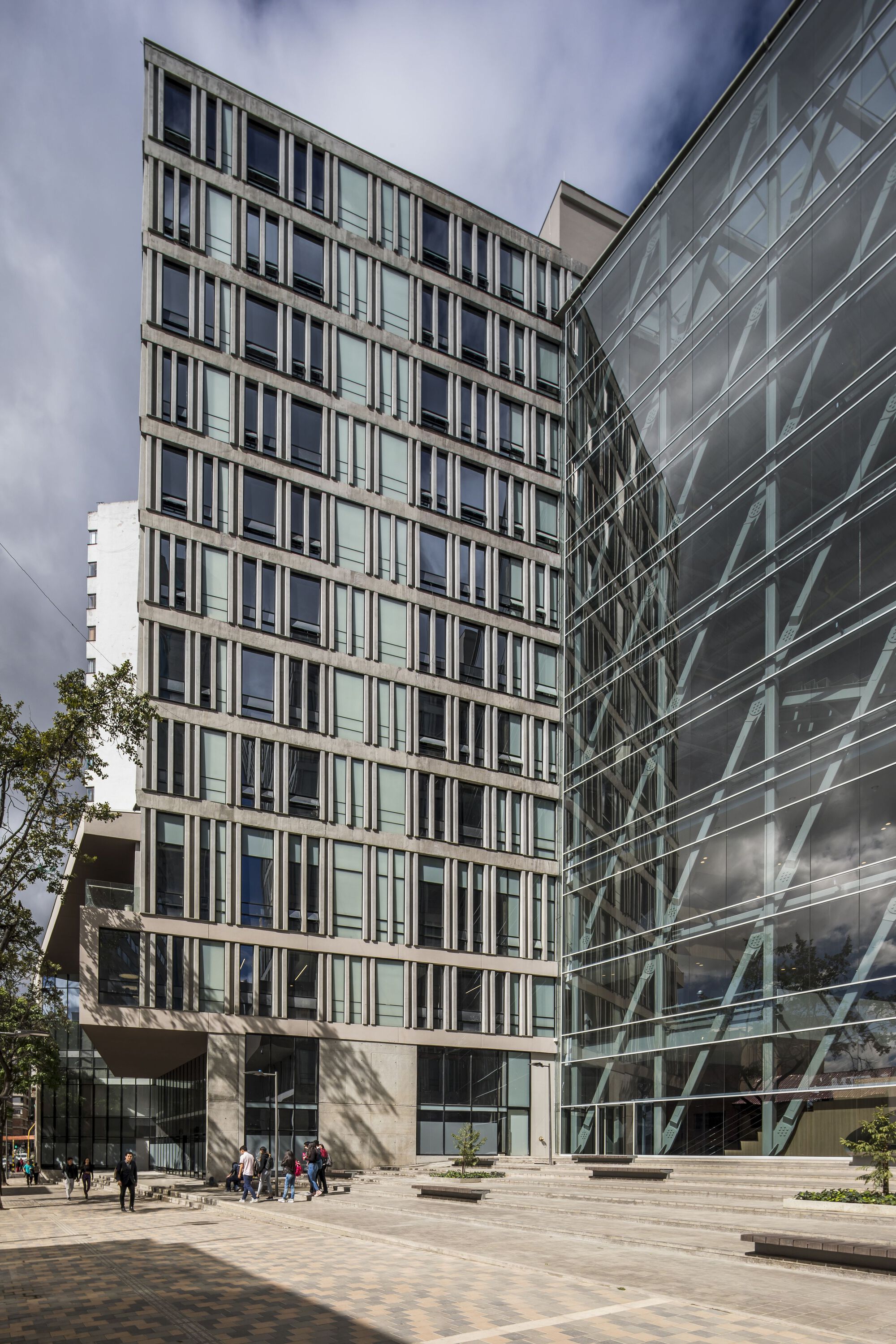 Corner view of the vertical window grid facade meeting the glass curtain wall under cloudy skies