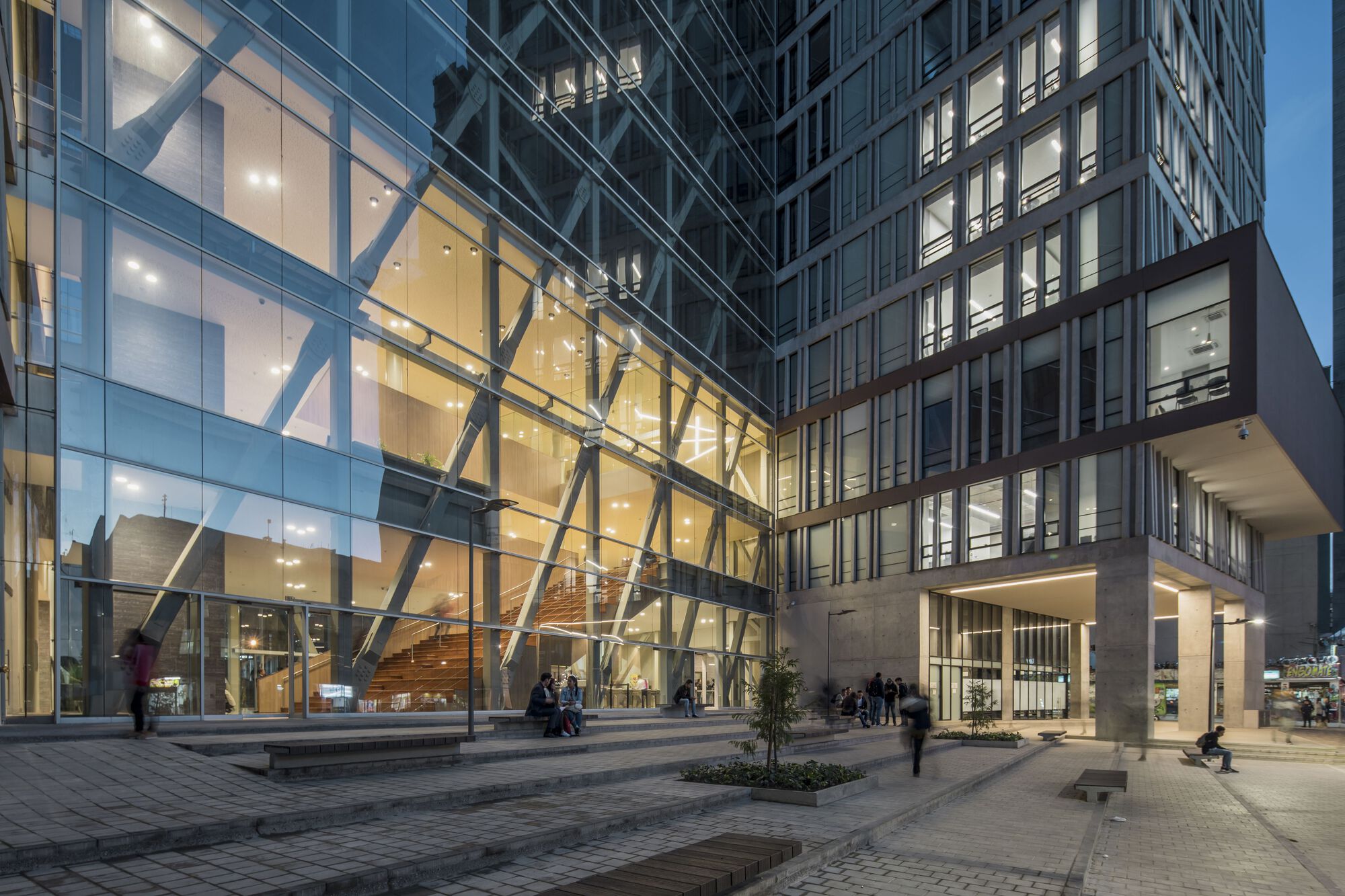 Glass entry pavilion with exposed diagonal bracing and illuminated interior staircase at twilight