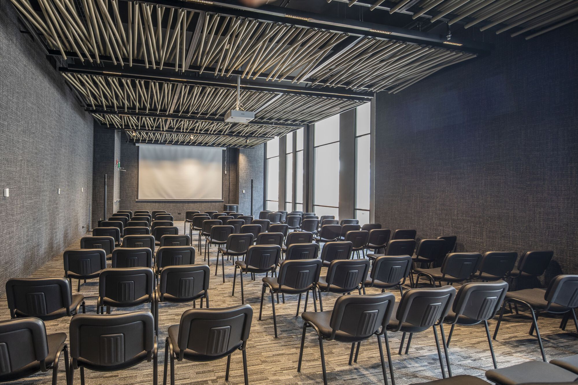 Auditorium with rows of black chairs under an exposed steel and wood batten ceiling