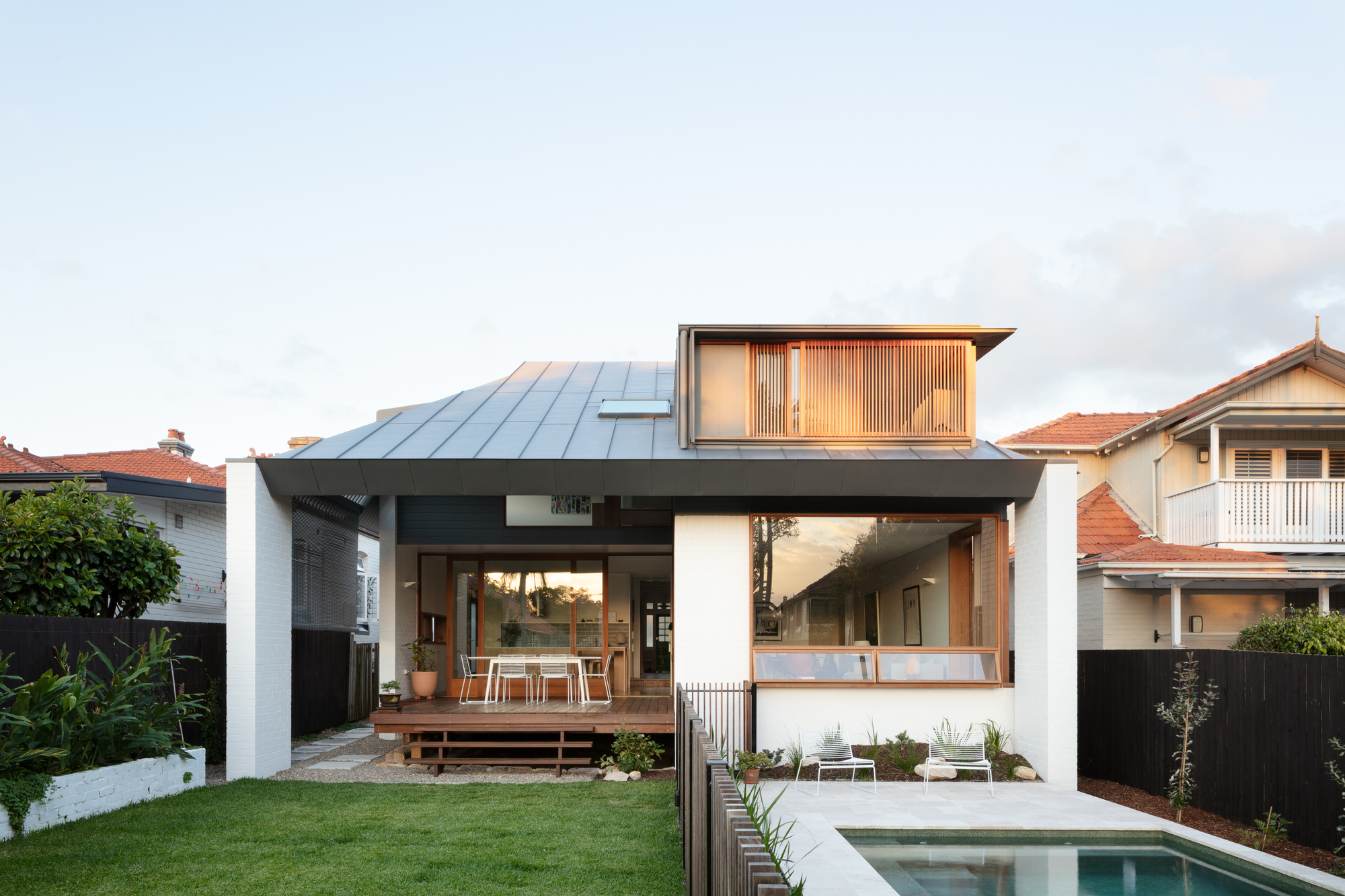 Rear facade with metal roof and timber screening above pool and lawn at dusk