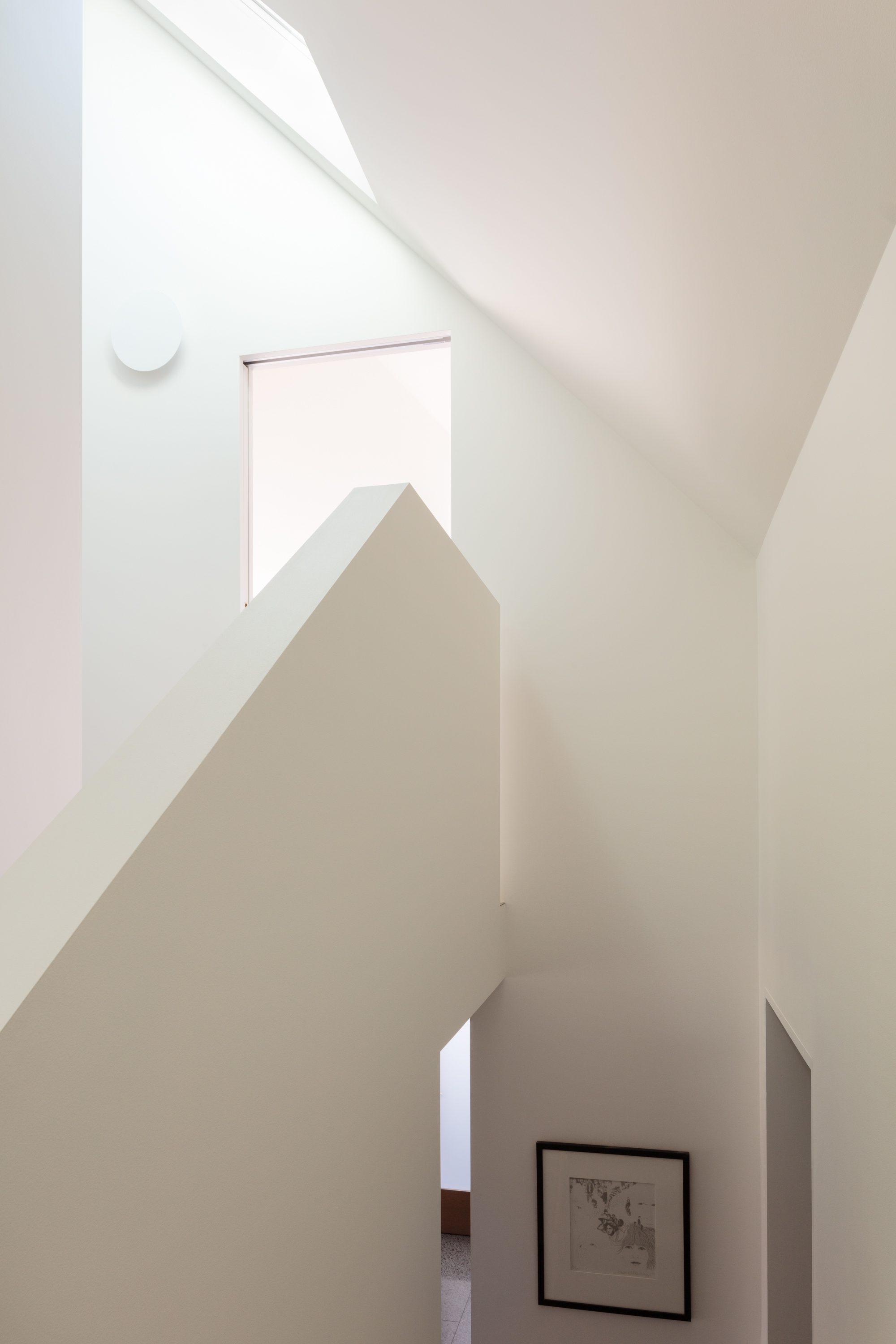 White stairwell with angled walls and a skylight casting diagonal shadows