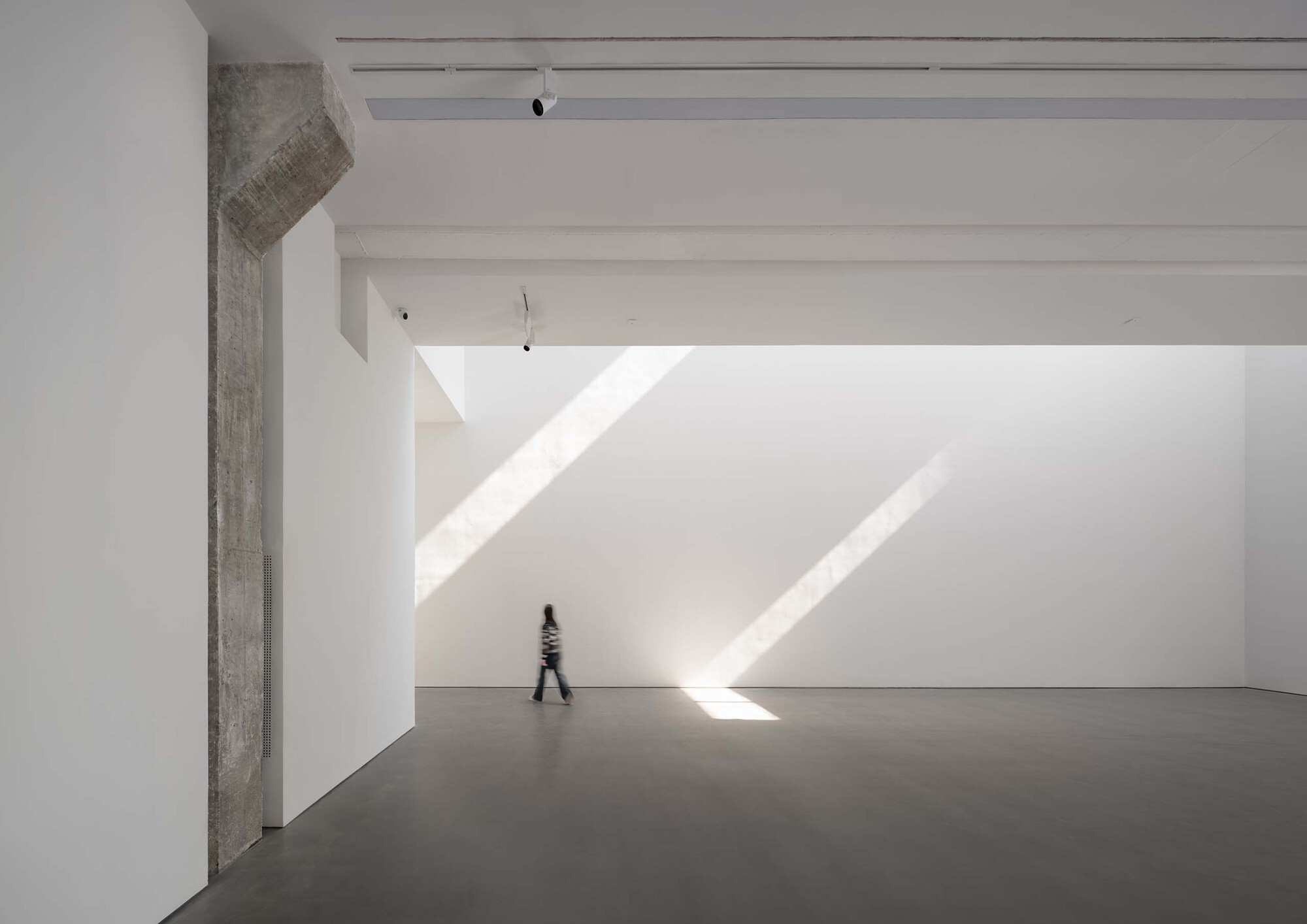 Gallery hall with raw concrete column and figure walking through diagonal sunlight on floor