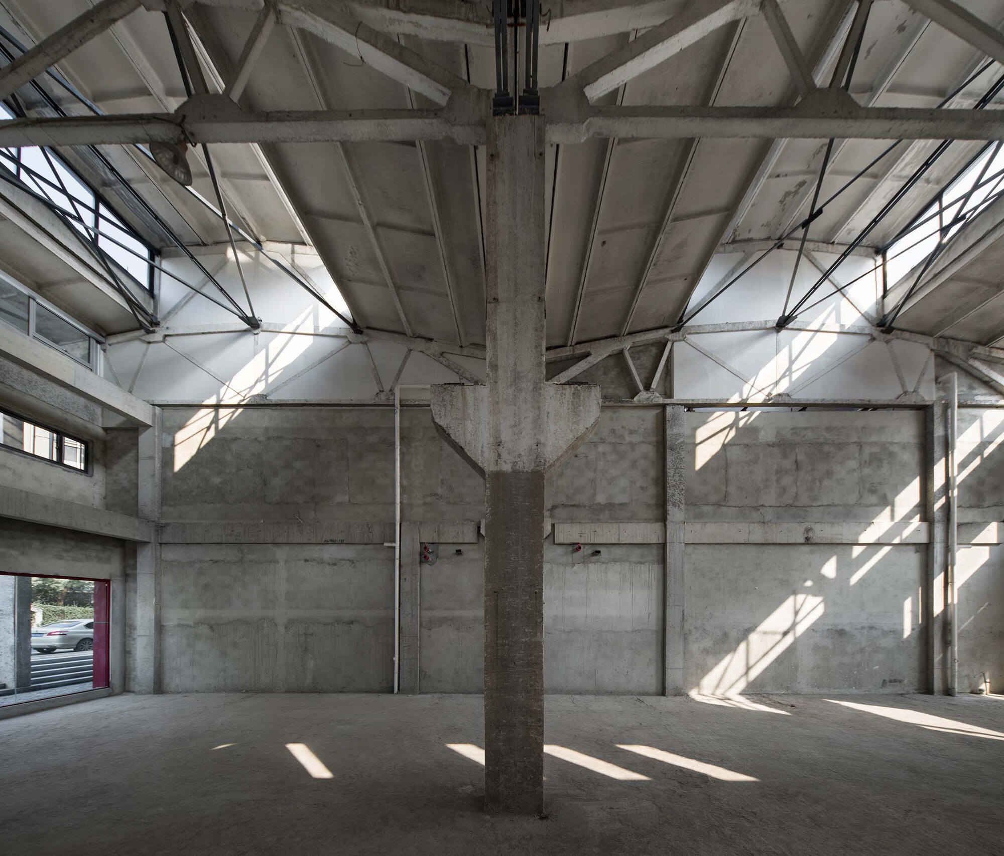 Exposed concrete structure with central column and steel roof trusses in bright natural light