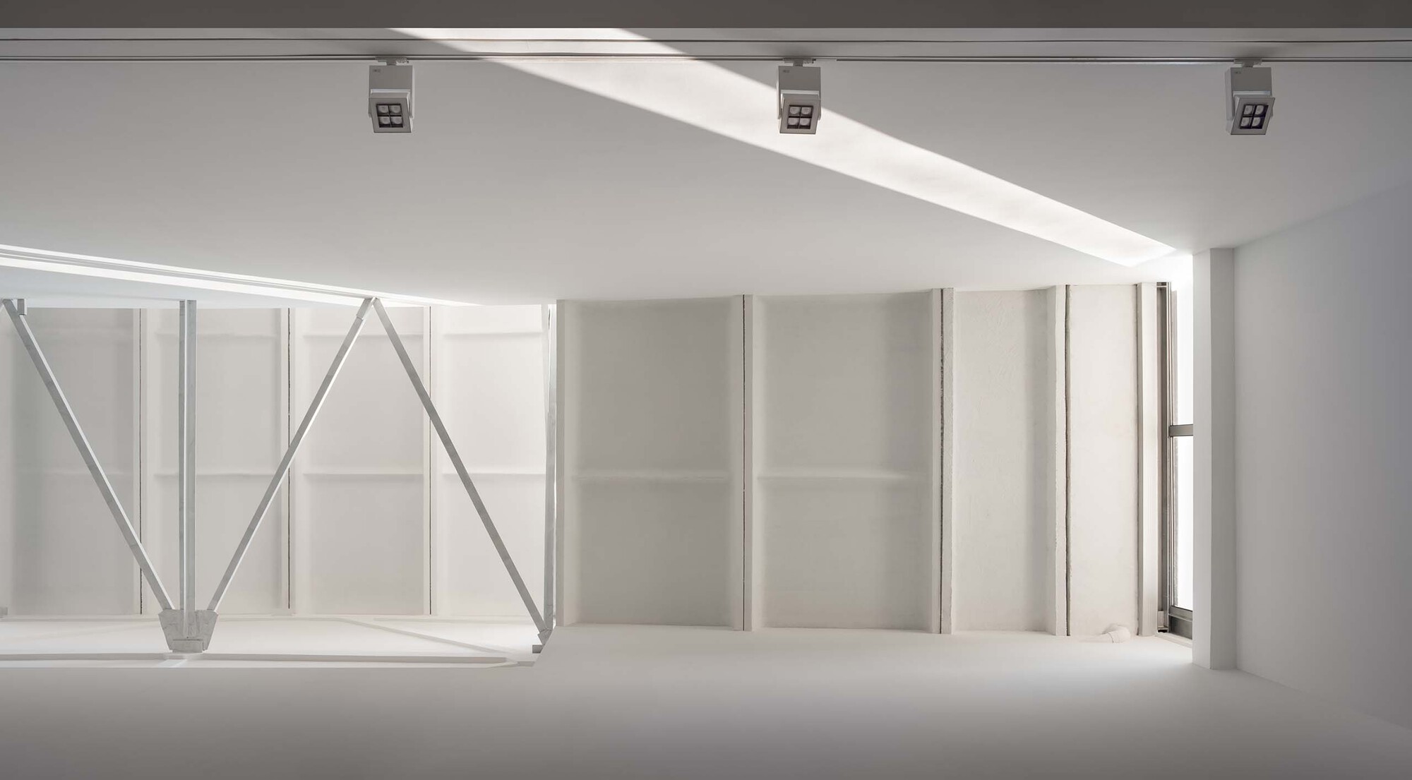 Gallery space with exposed steel truss structure and white partition walls below a clerestory