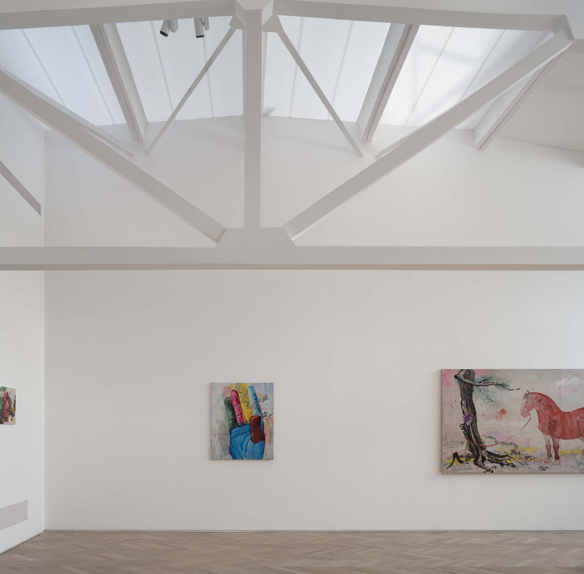 Interior gallery with exposed steel roof trusses and skylights above paintings on white walls
