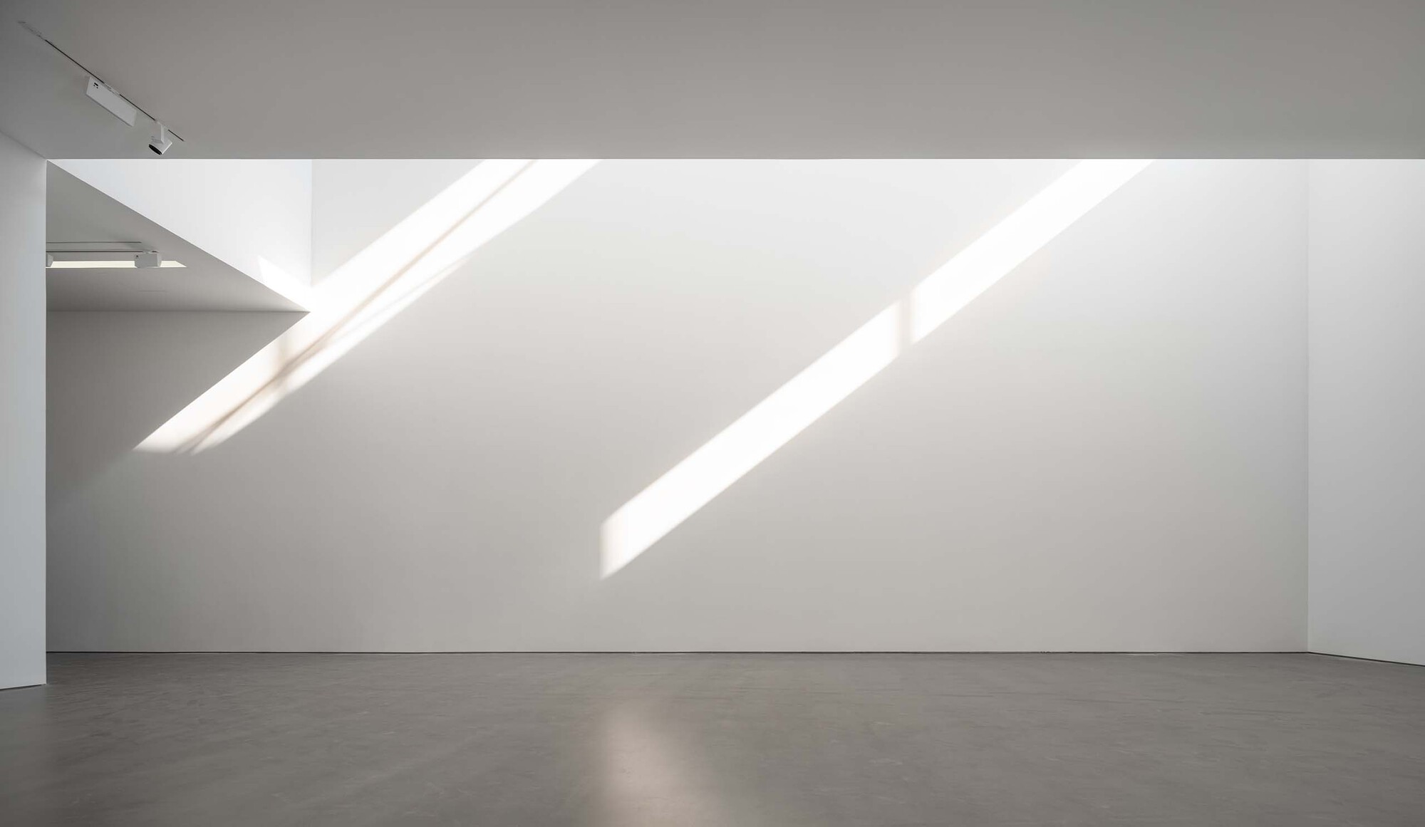 Gallery corner with diagonal skylights casting parallel bands of sunlight on the white wall