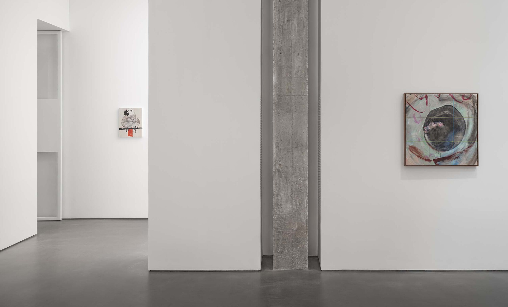 Gallery space with exposed concrete beam dividing white walls hung with framed artworks