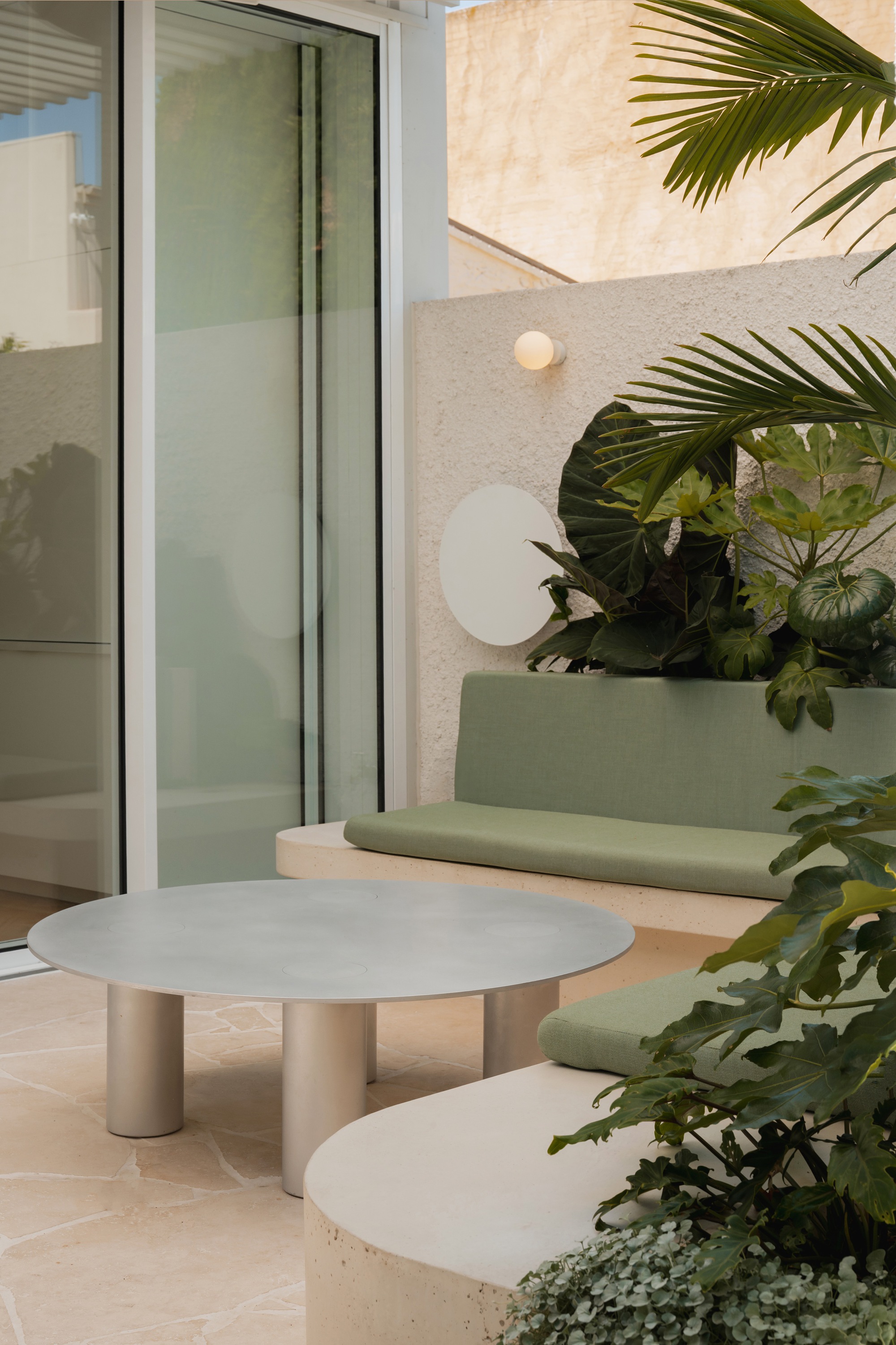 Courtyard terrace with pale stone table and built-in sage green bench beside tropical planting