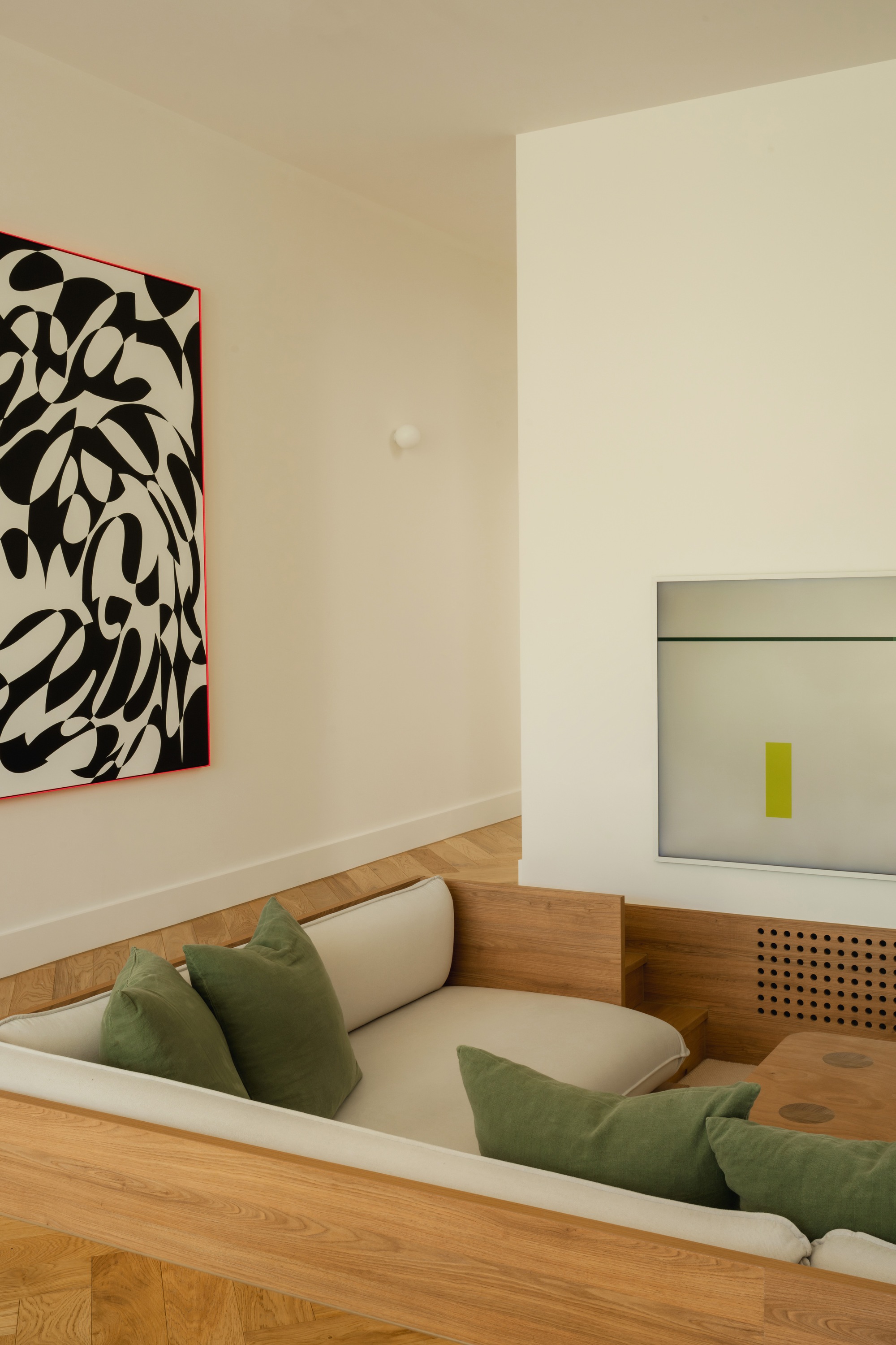 Sunken seating area with timber flooring and green cushions beneath a large abstract artwork