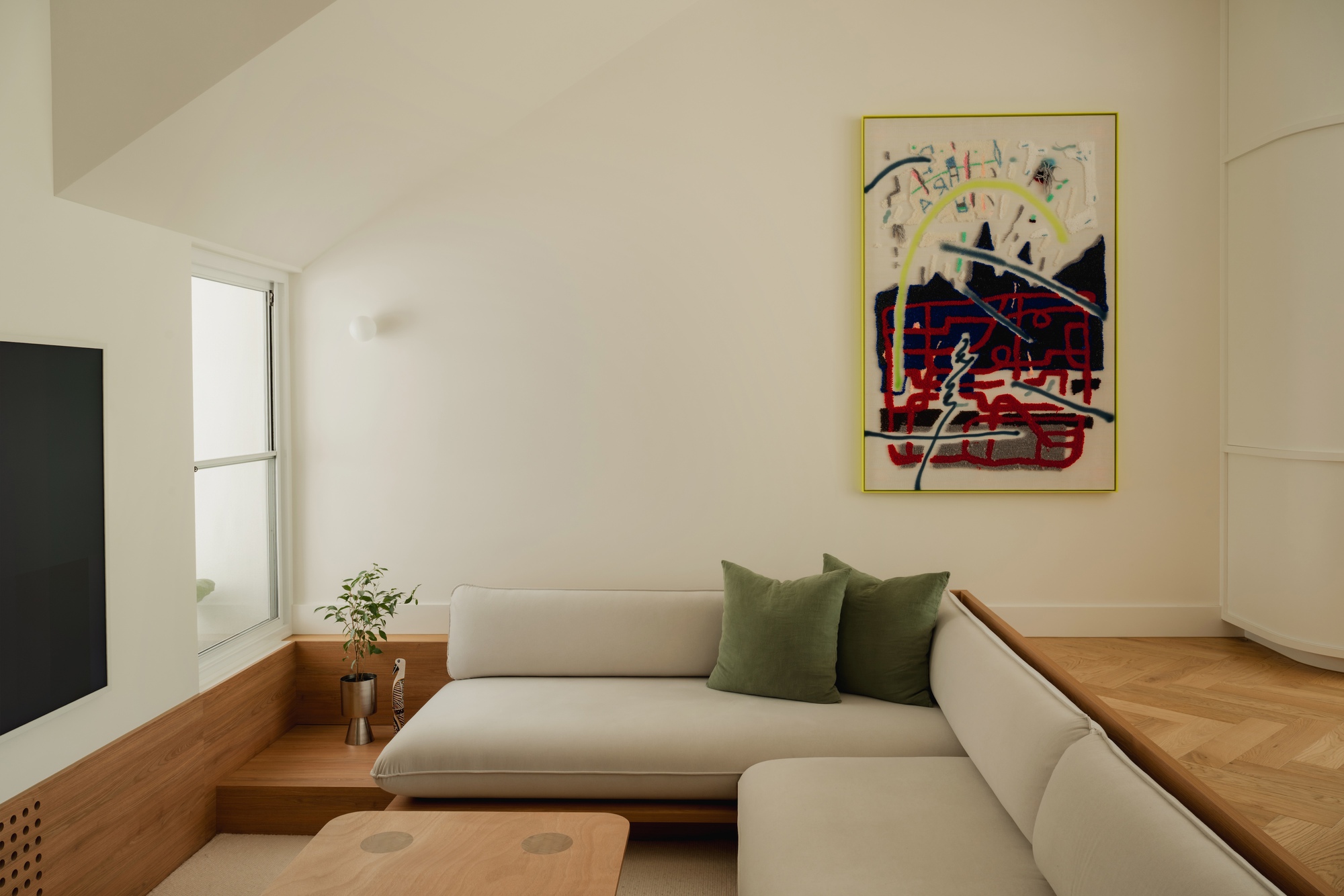 Corner sofa with integrated timber platform and colorful framed artwork on wall