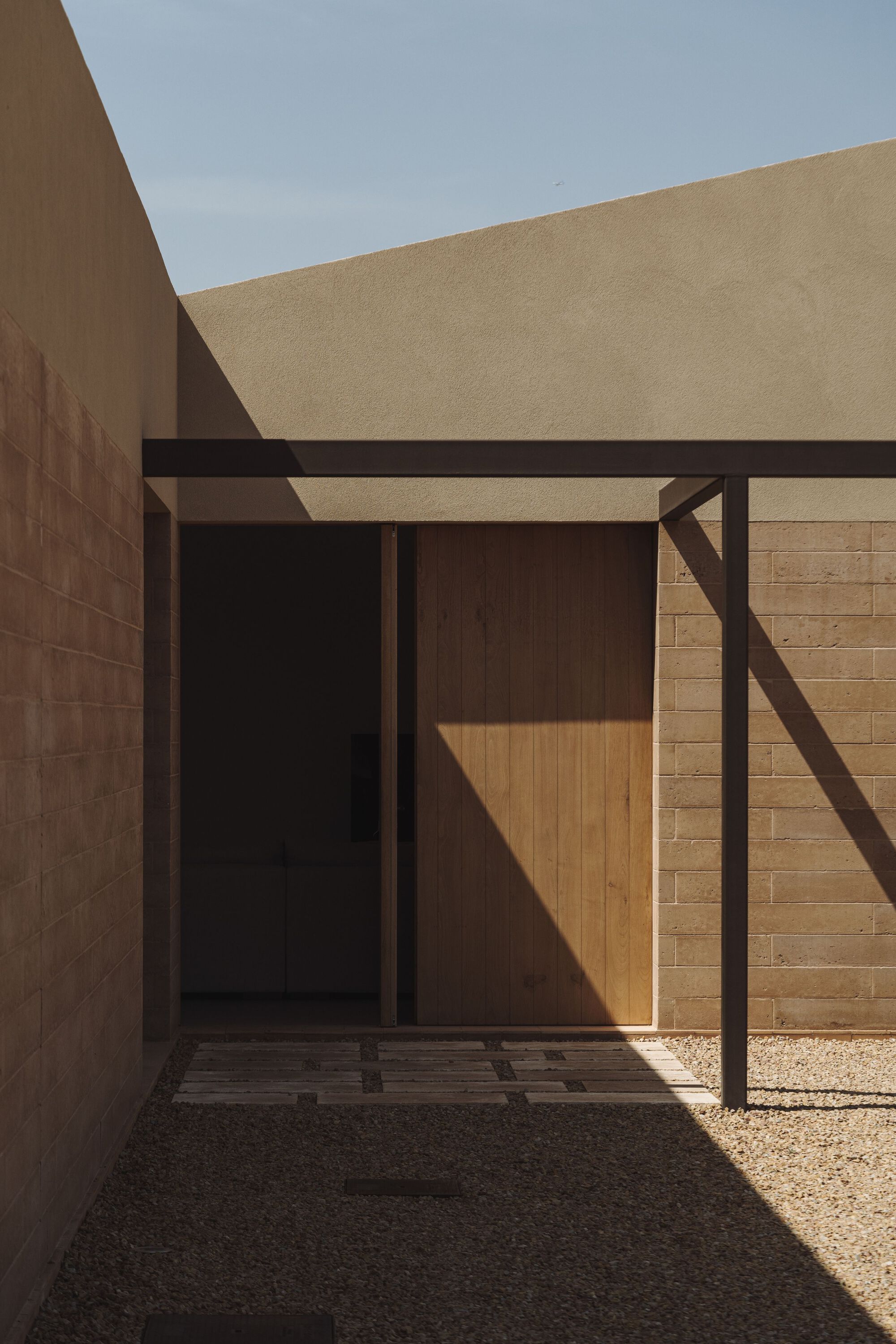 Entry portal with steel frame and timber door caught in afternoon light within courtyard walls