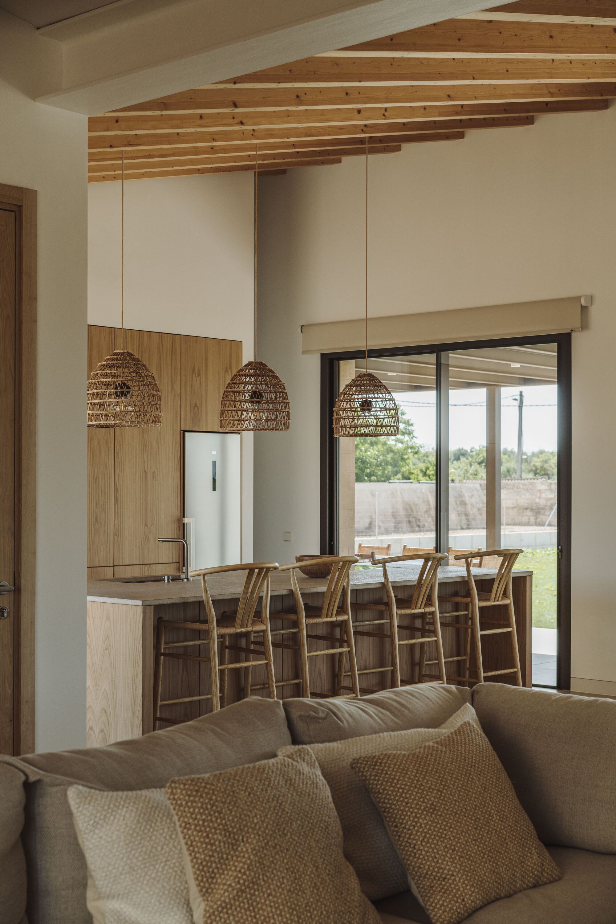 Open-plan living area with exposed timber ceiling beams and kitchen island beneath woven pendant lights