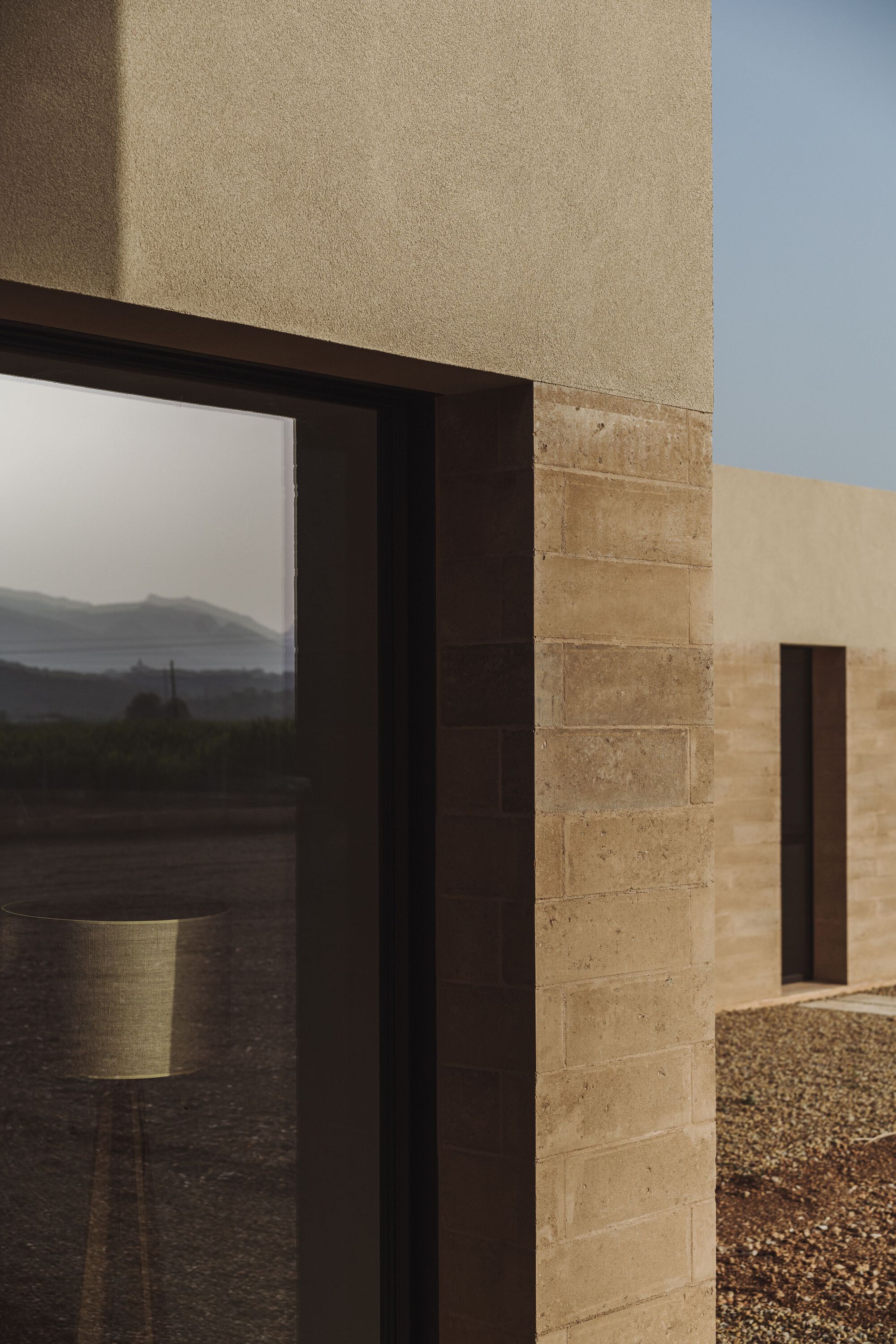 Corner detail of stacked stone masonry meeting a dark metal window frame at dusk