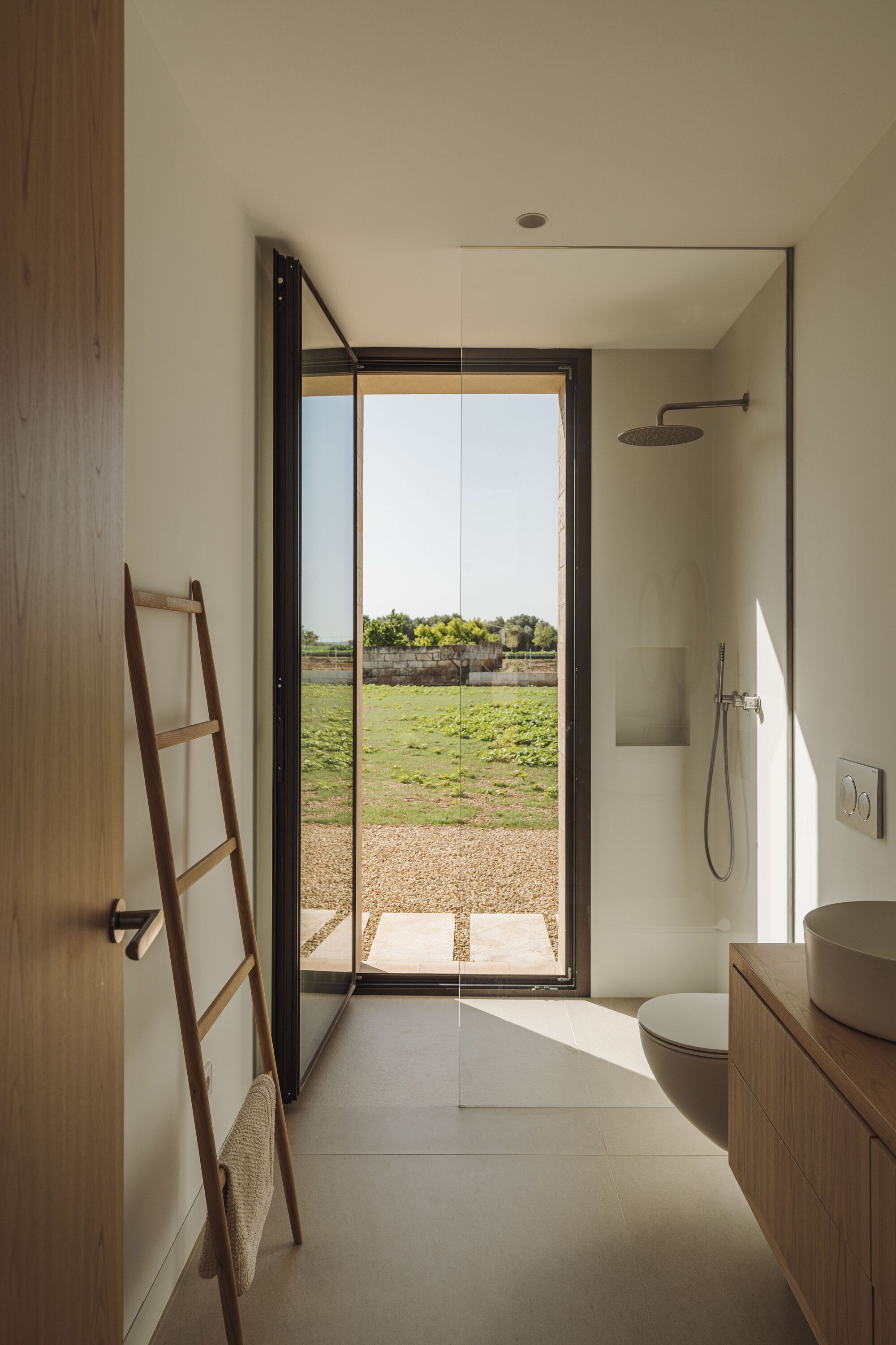 Bathroom with black-framed glass door opening to a gravel terrace and green field beyond