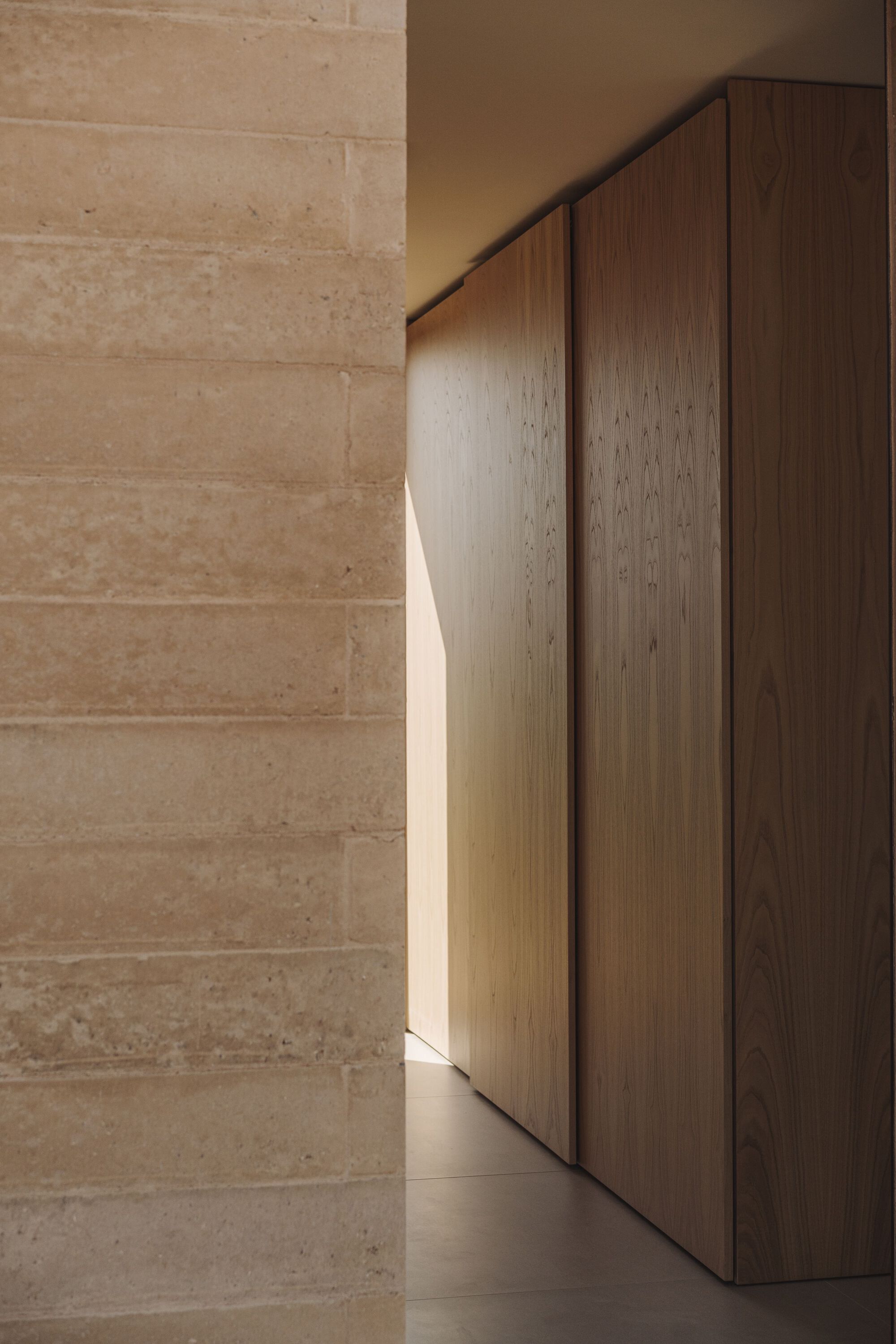 Close-up of timber cabinetry meeting a rammed earth wall in soft natural light
