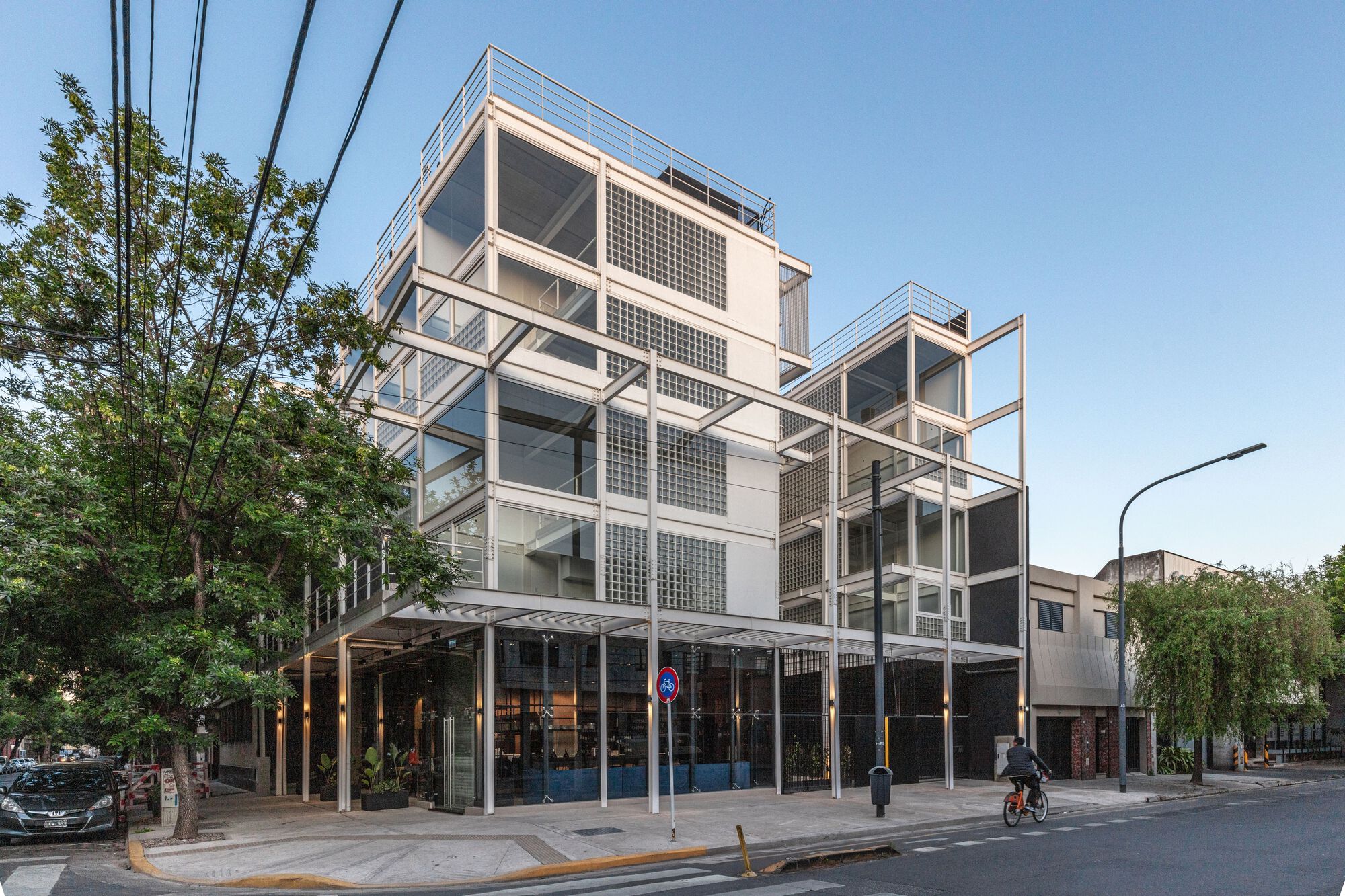 Street view of the white steel frame facade with glass block panels and cantilevered balconies at dusk