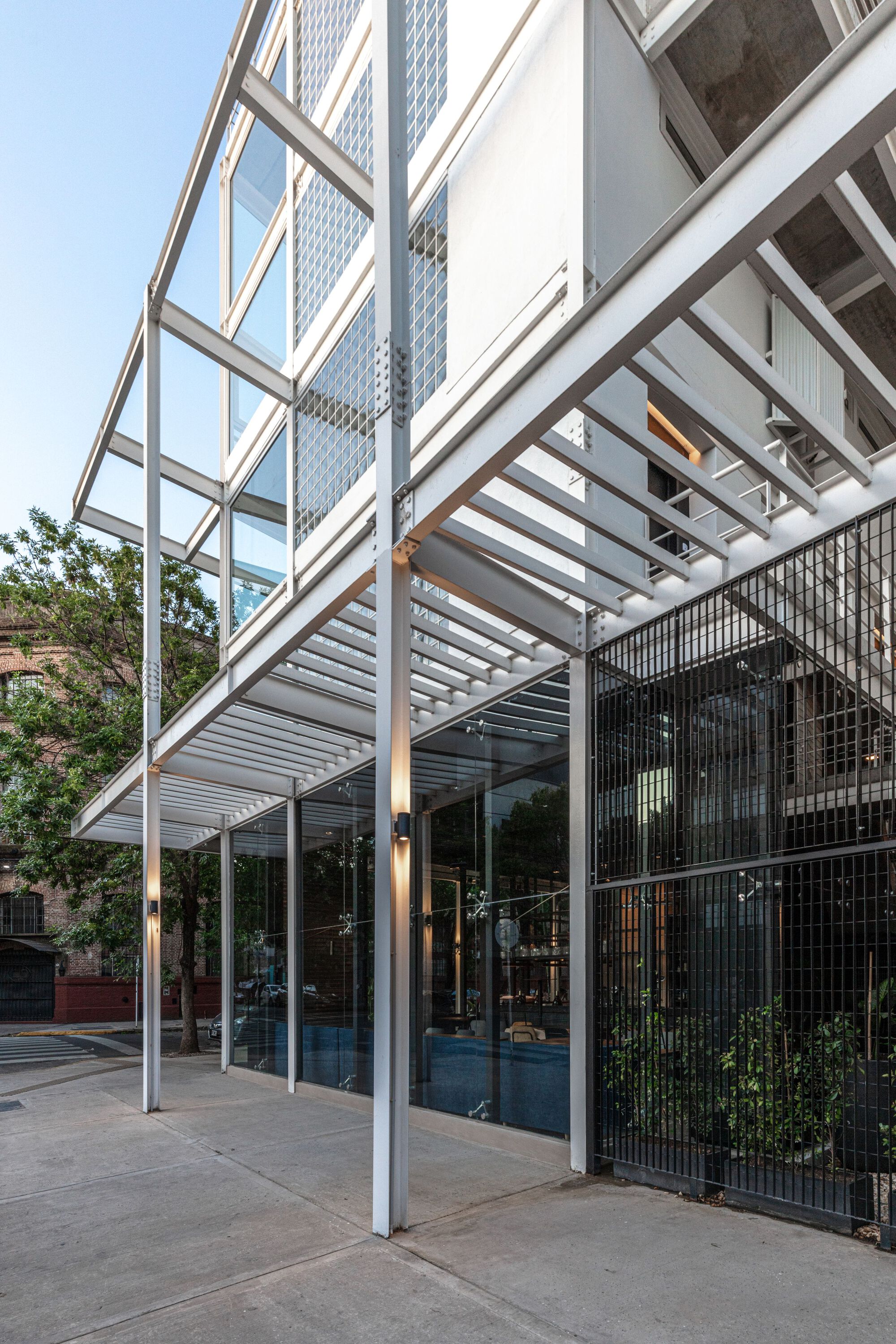 Ground level covered entry with steel pergola structure and vertical metal bar screens beside planted areas