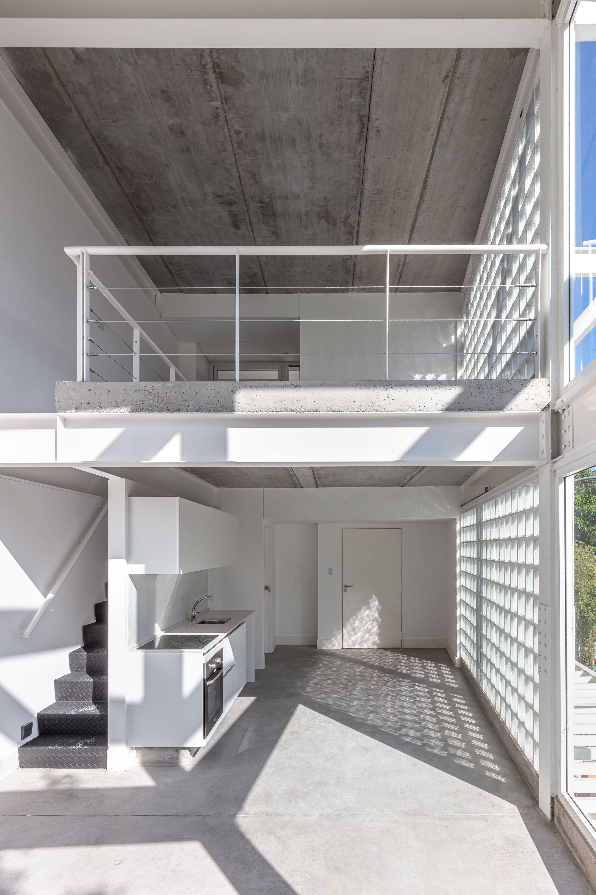Double height interior space with mezzanine, exposed concrete ceiling and kitchen beneath upper level railing