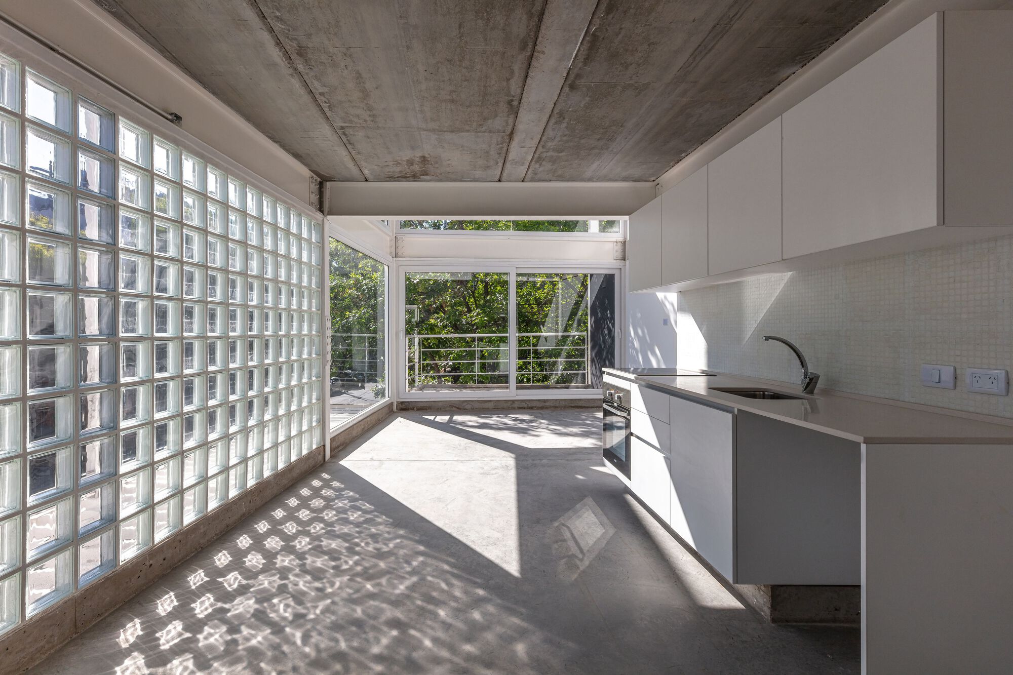 Interior kitchen with glass block wall casting dappled shadows on polished concrete floor