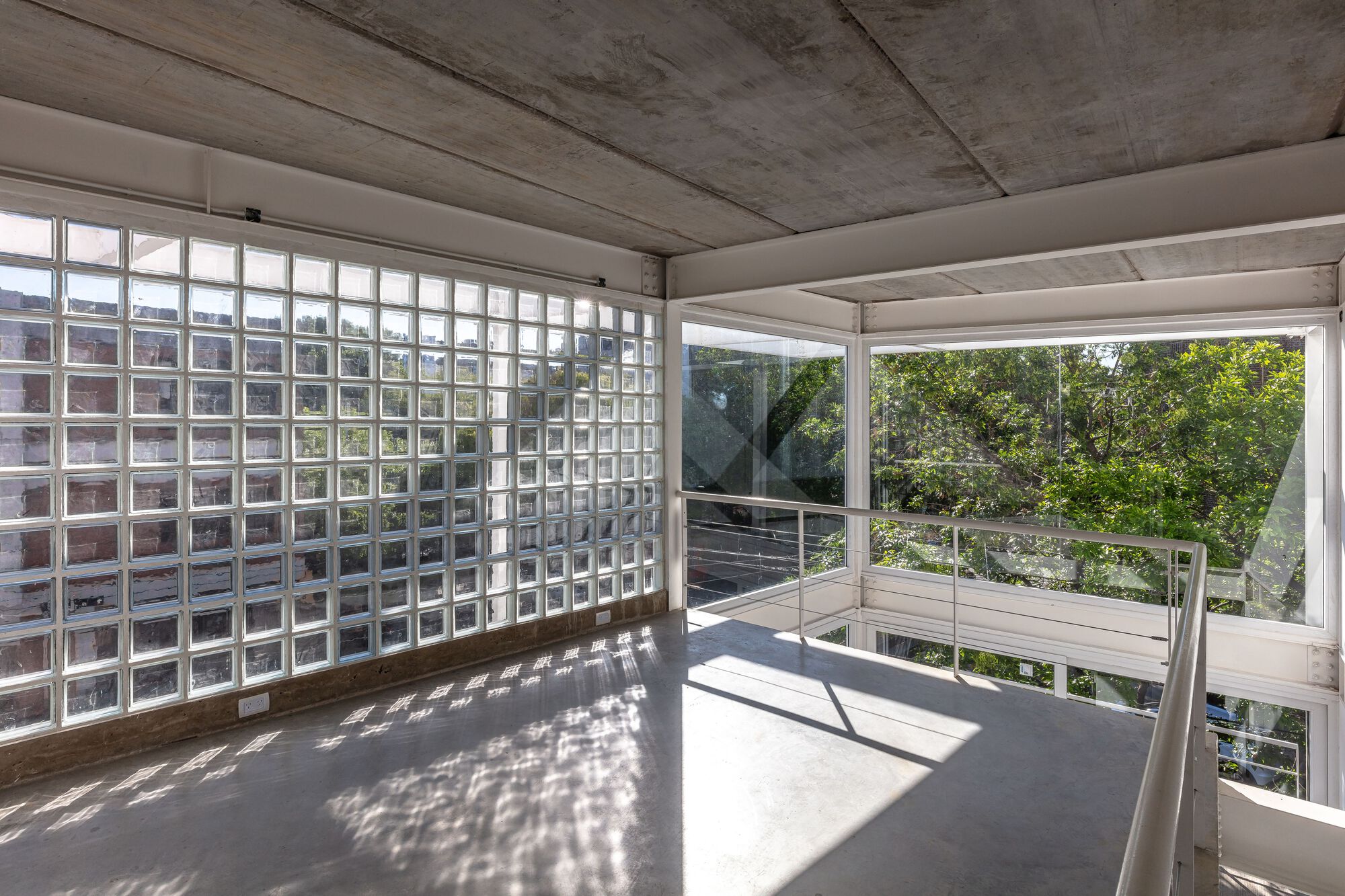 Corner terrace with glass block wall and cable railing overlooking trees in sunlight