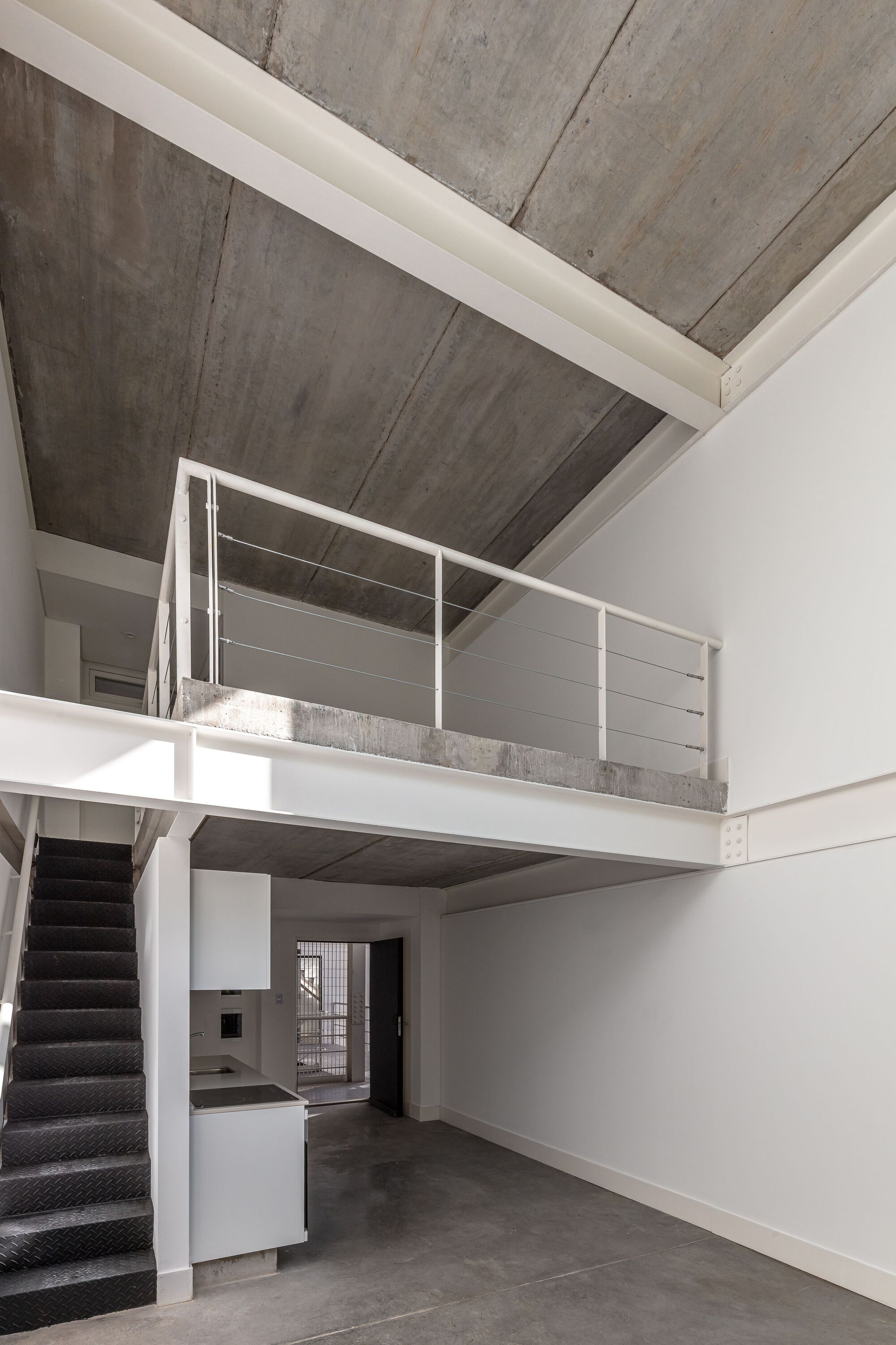 Double-height interior with mezzanine, exposed concrete ceiling and metal railing